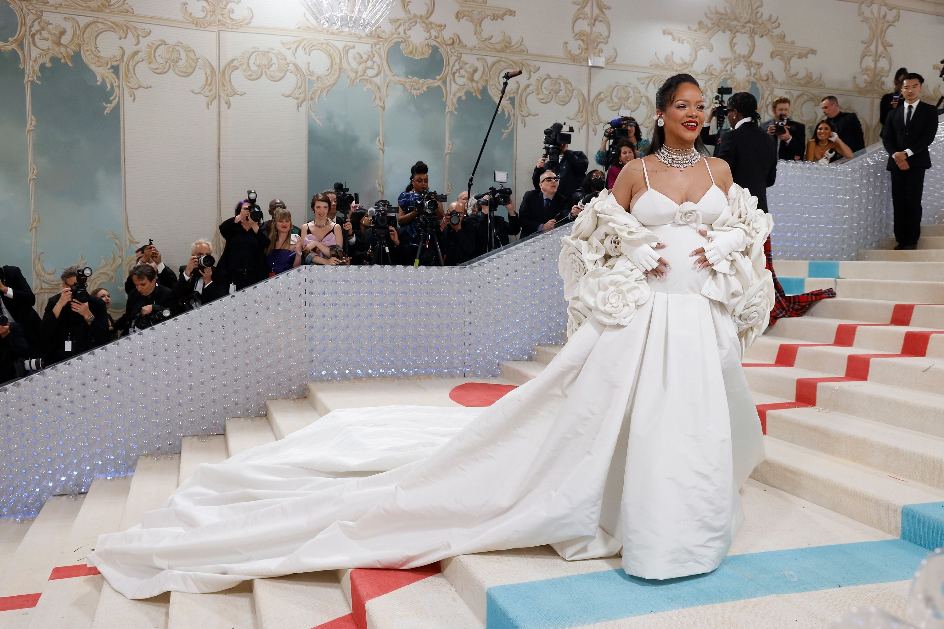 Frau in weißem Kleid mit langer Schleppe posiert auf einer Treppe vor Fotografen bei einer Gala.