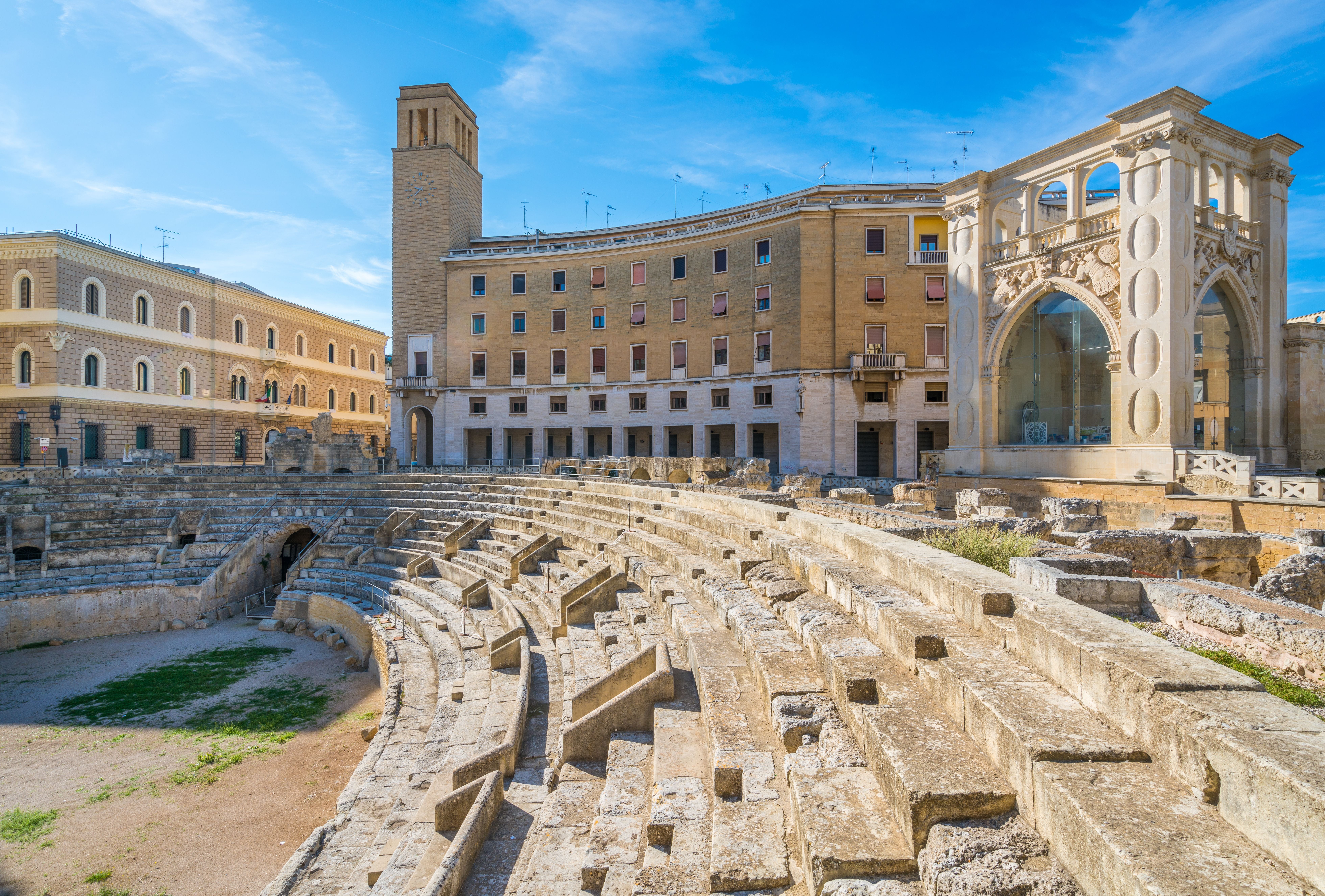 Römisches Amphitheater in Lecce, umgeben von historischen Gebäuden bei blauem Himmel.