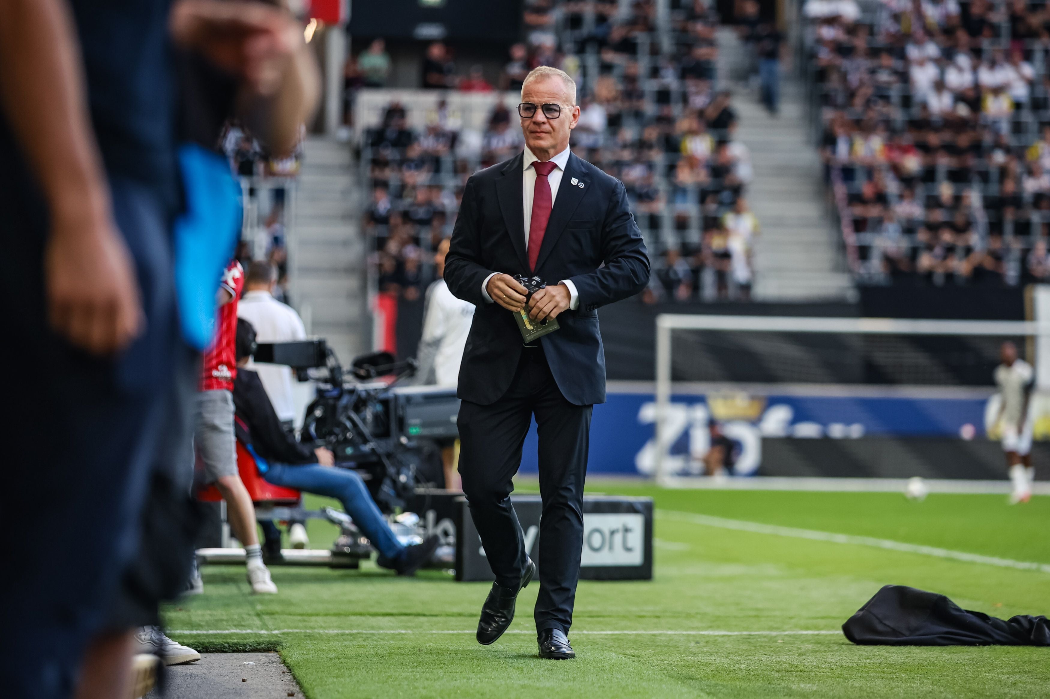 LASK-Präsident Siegmund Gruber geht im dunklen Anzug mit roter Krawatte am Spielfeldrand entlang.