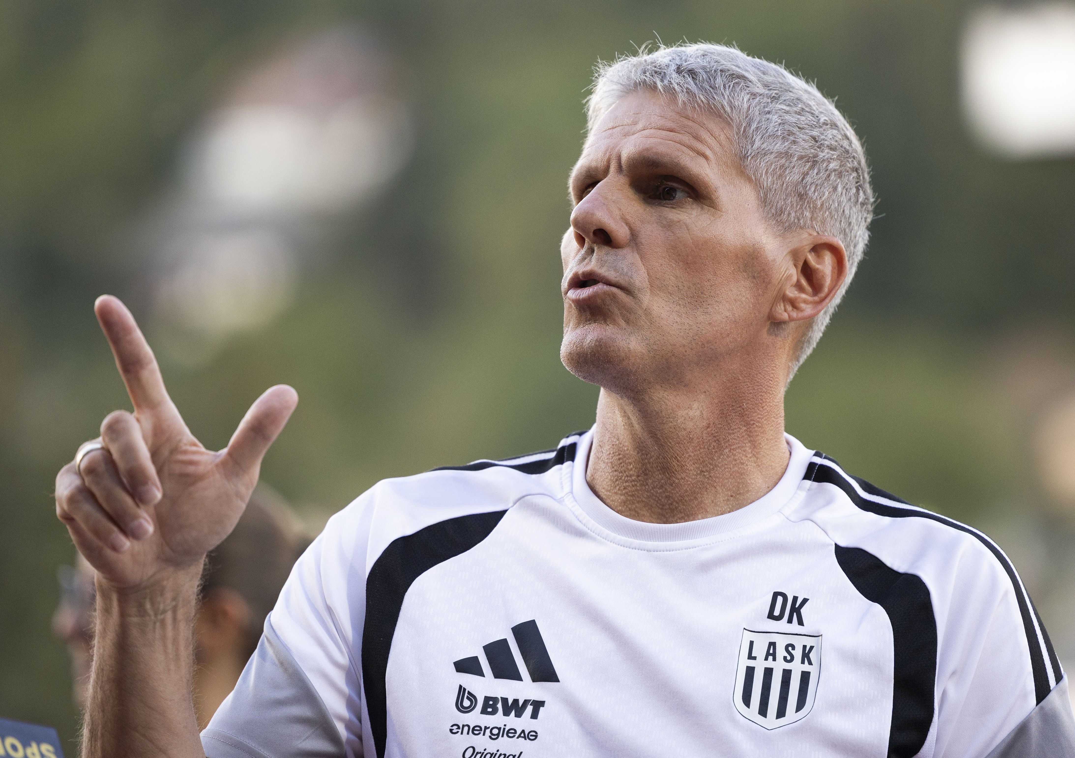 Ein Trainer mit grauen Haaren und LASK-Poloshirt gestikuliert beim Fußballspiel.