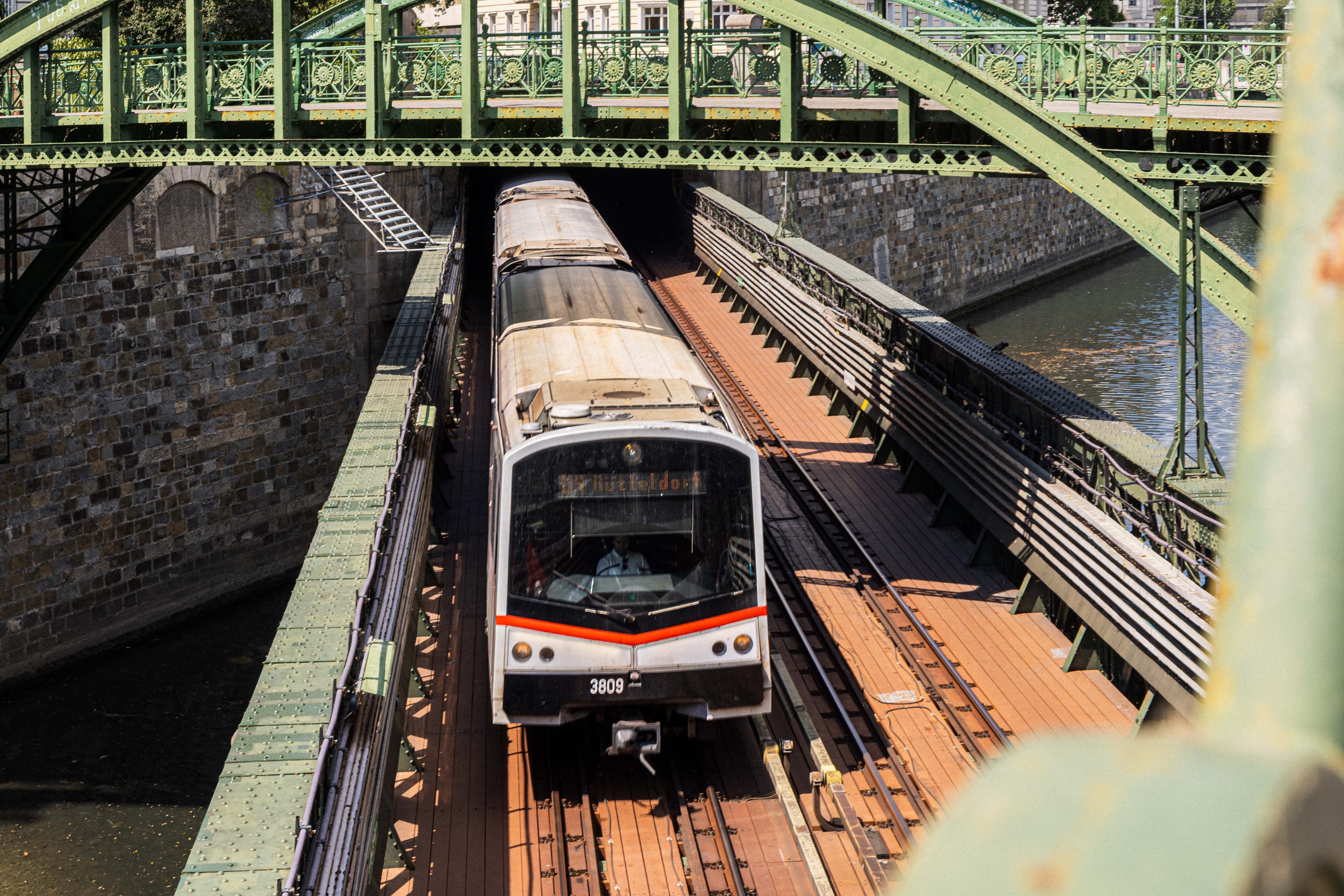 U-Bahn-Zug fährt unter einer grünen Eisenbrücke auf einer Brücke über einen Kanal.