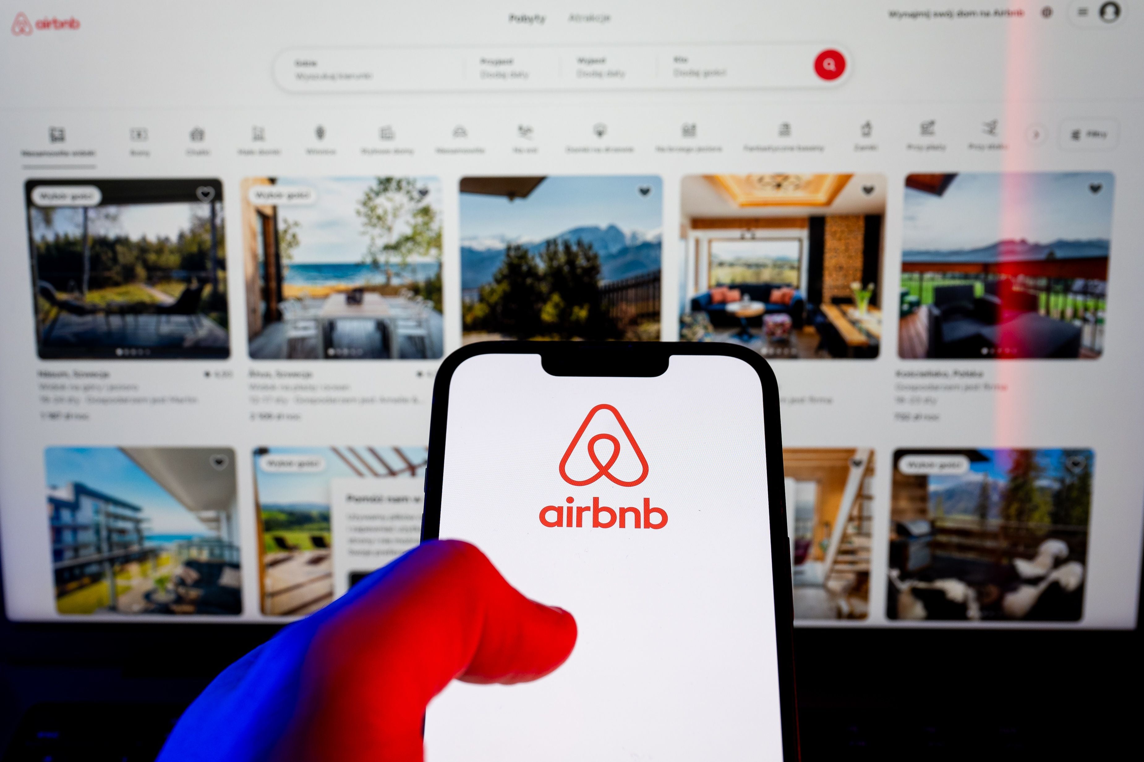 Airbnb-Logo auf Smartphone, im Hintergrund die Airbnb-Website mit verschiedenen Unterkünften.