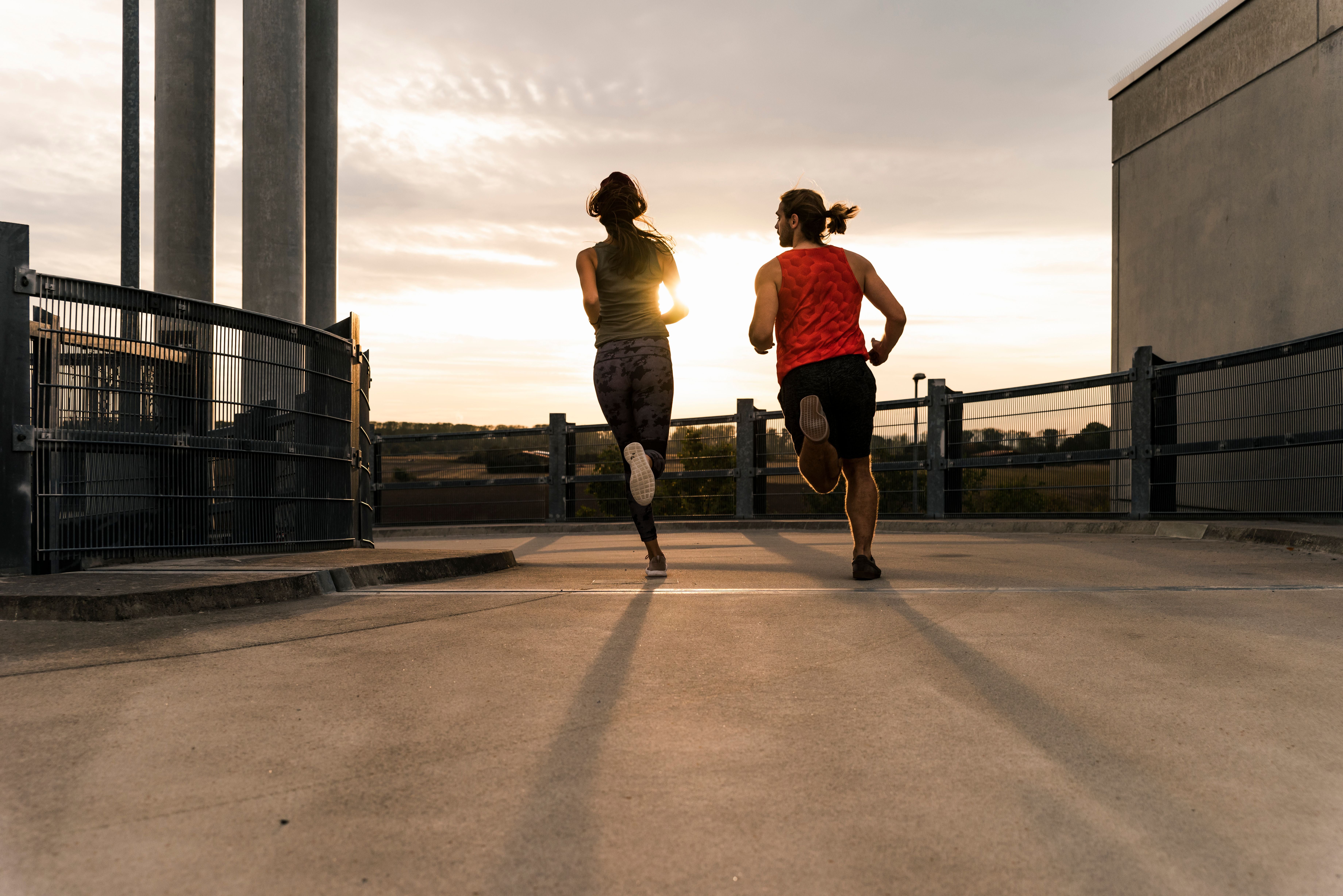 Zwei Personen joggen bei Sonnenuntergang auf einer Betonfläche mit Geländer.