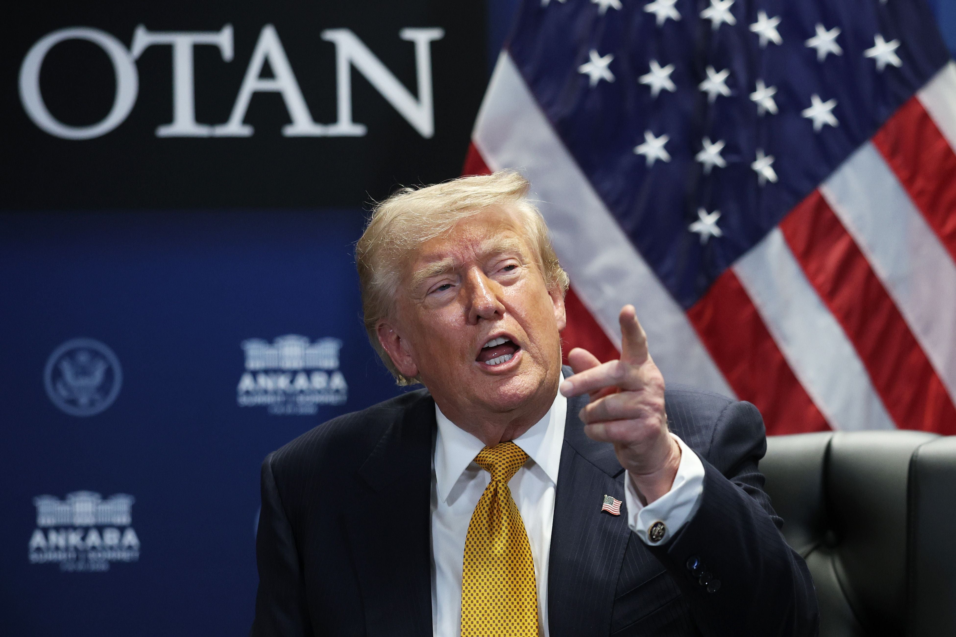 Donald Trump gestikuliert während eines Treffens vor einer US-Flagge und dem NATO-Logo.
