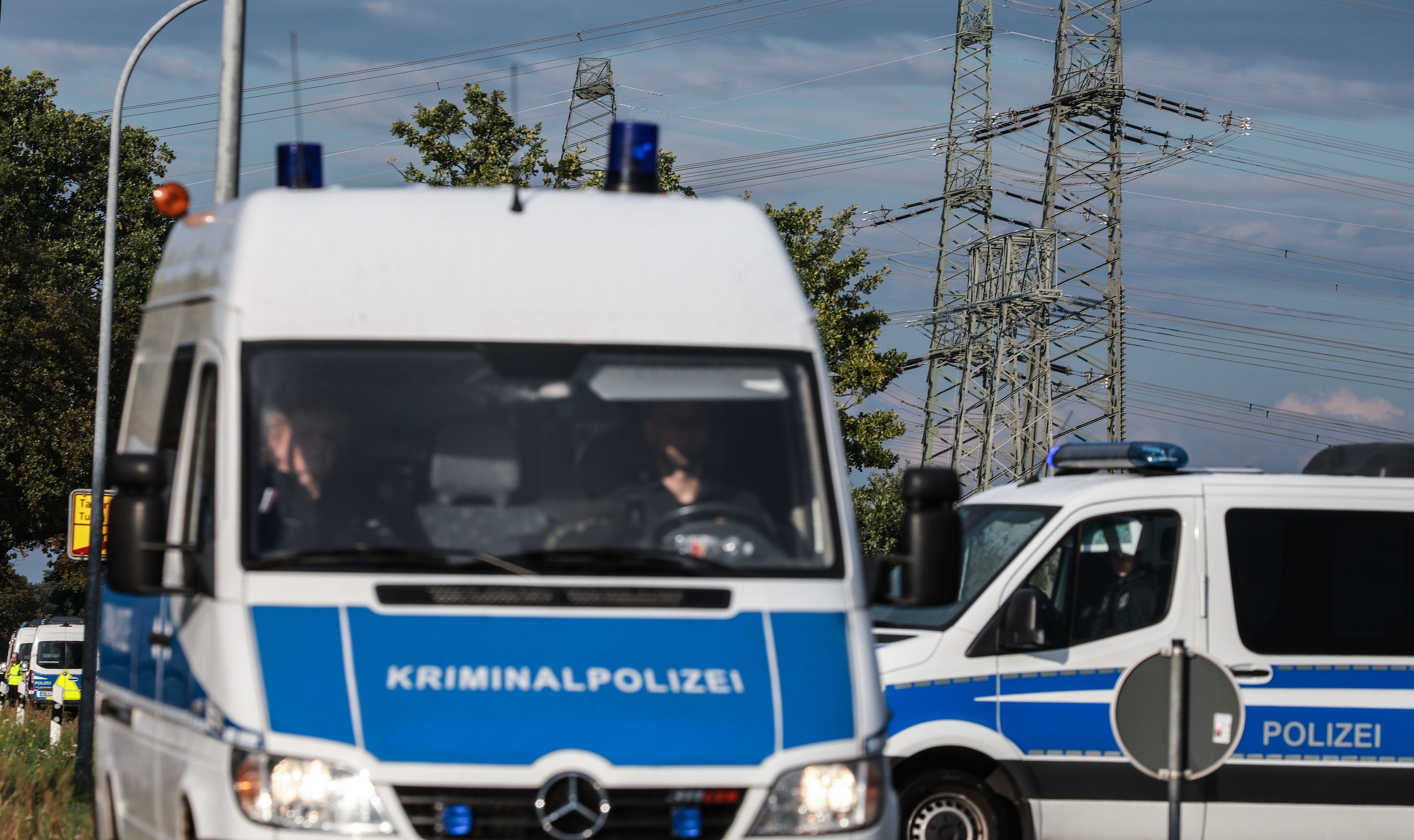 Polizeifahrzeuge sperren eine Straße bei einem Umspannwerk, Strommasten im Hintergrund.