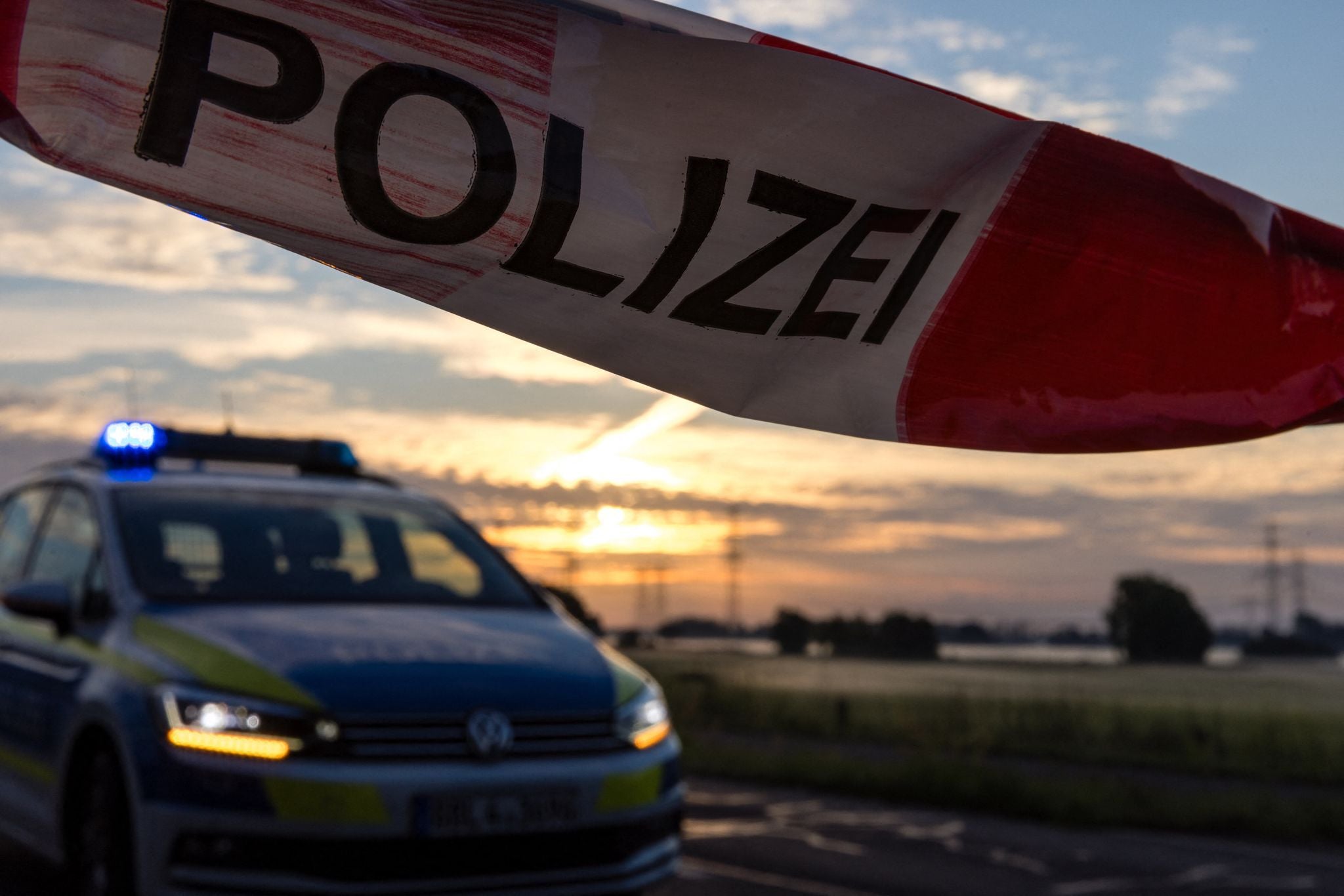 Absperrband mit "Polizei" vor einem Polizeiwagen bei Sonnenaufgang, ländliche Umgebung.