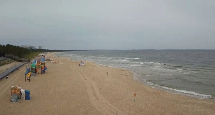 Weiter Sandstrand an der Ostsee mit vereinzeltem Spielplatz und ruhigem Meer bei bewölktem Himmel.