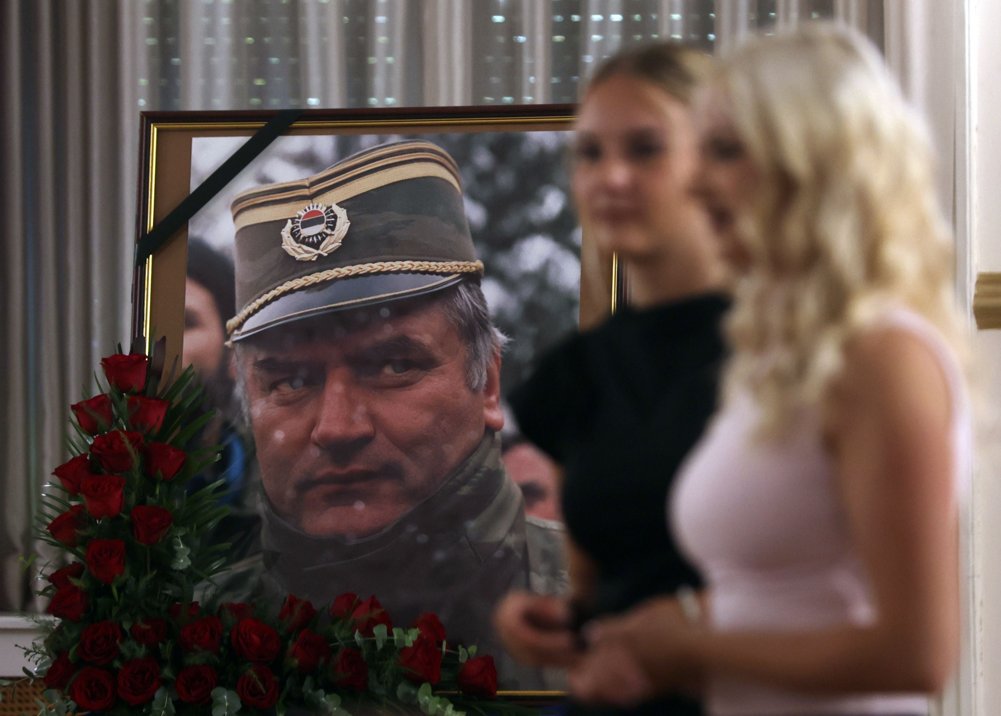 Zwei Frauen gehen an einem mit Rosen geschmückten Porträt eines Generals vorbei.