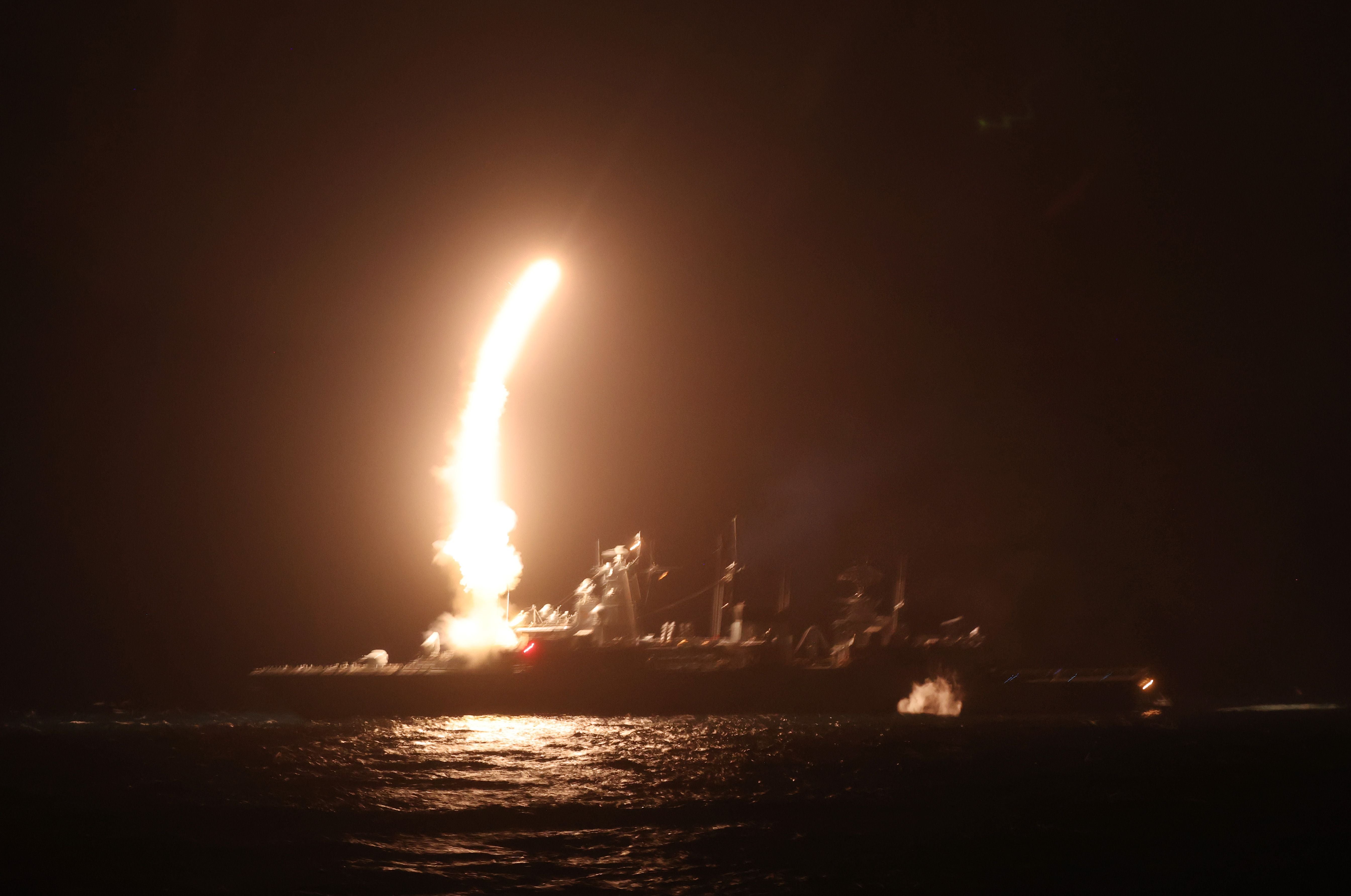 Ein Kriegsschiff feuert nachts im Meer eine leuchtende Rakete ab.