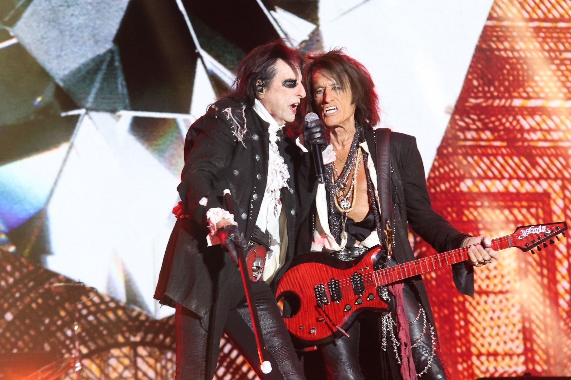 Zwei Musiker der Hollywood Vampires rocken mit Mikrofon und roter Gitarre auf der Bühne.