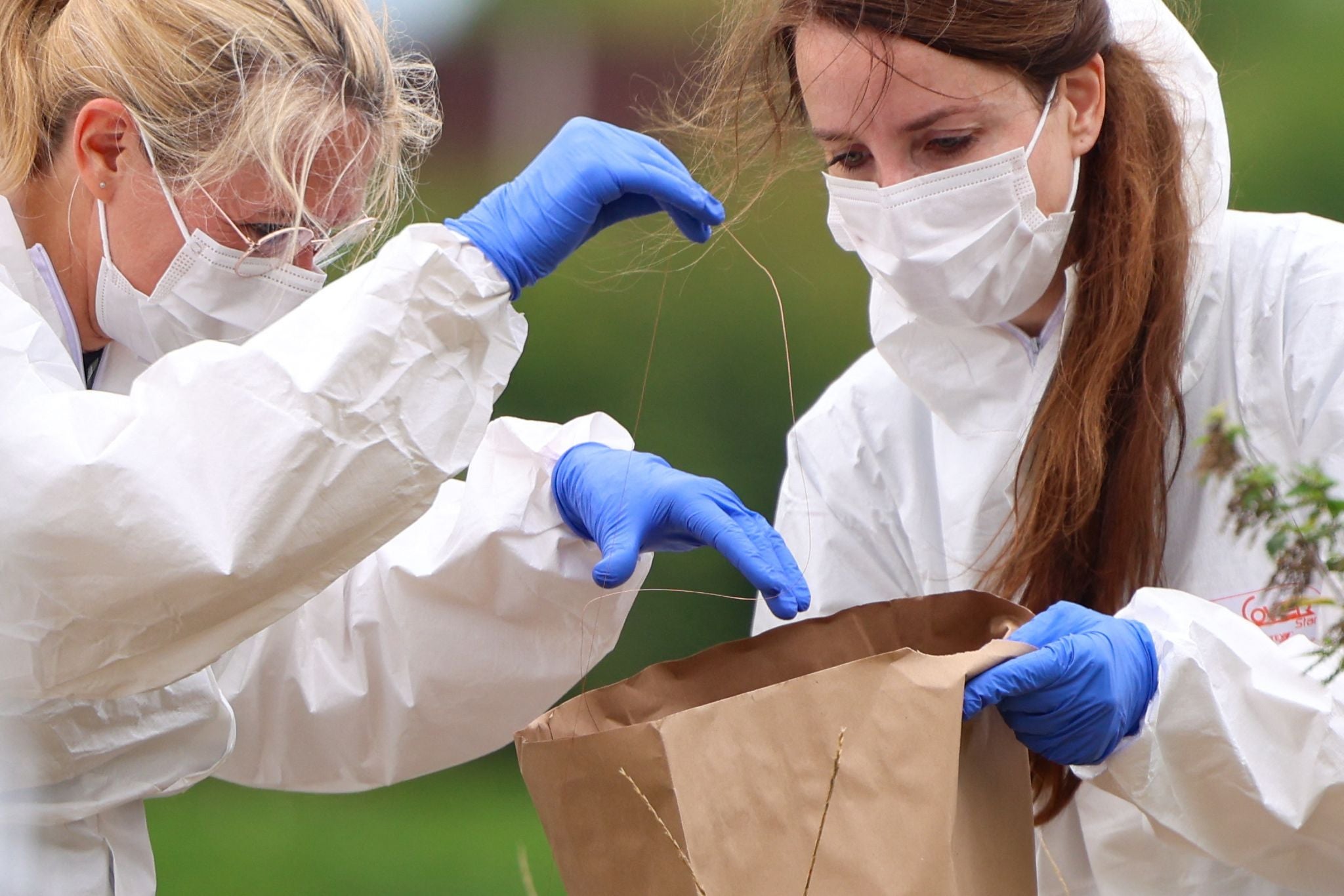 Zwei Kriminaltechnikerinnen sichern mit Schutzanzügen und Handschuhen Spuren in einer Papiertüte.