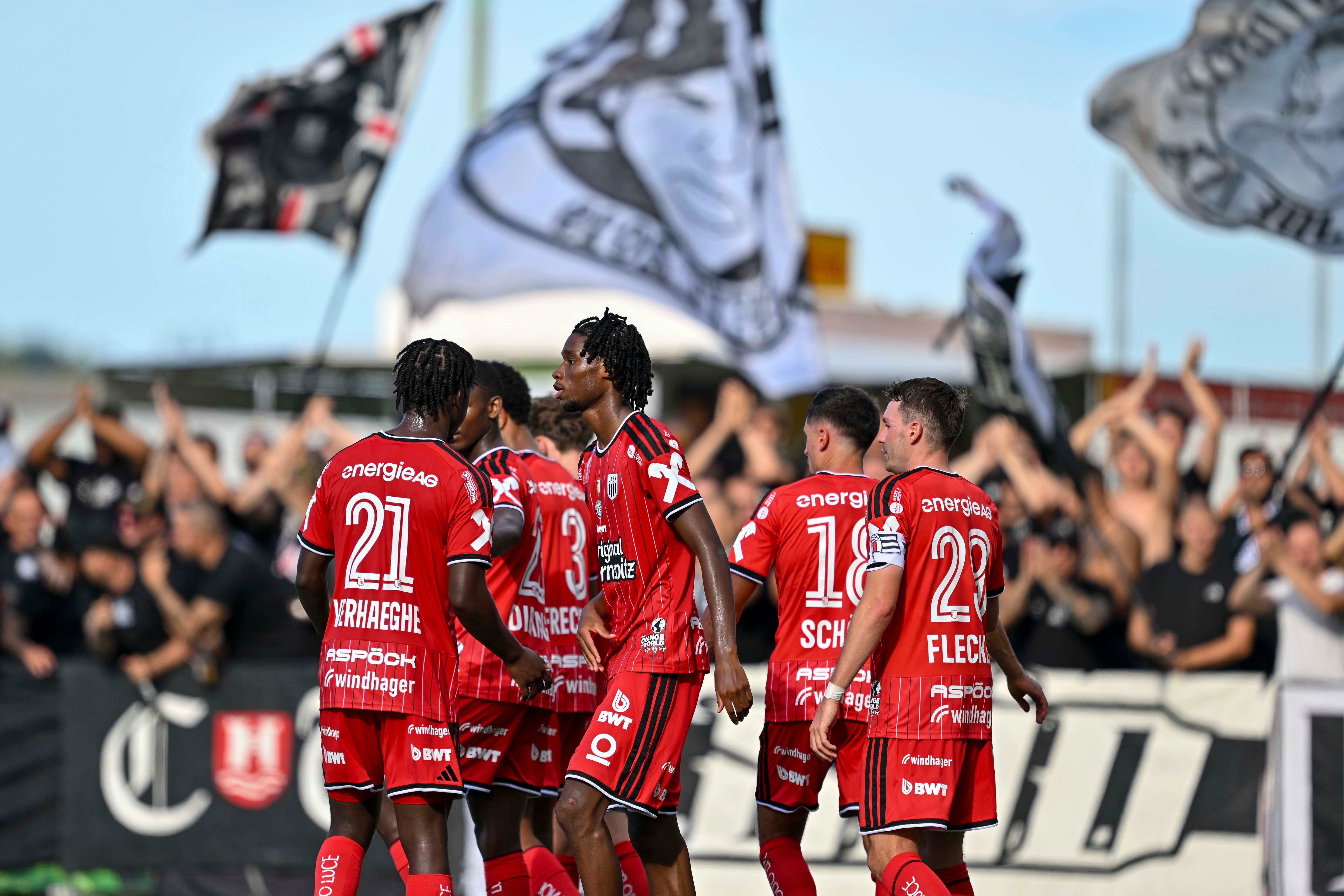 LASK-Spieler feiern im roten Trikot vor jubelnden Fans und geschwenkten Fahnen.