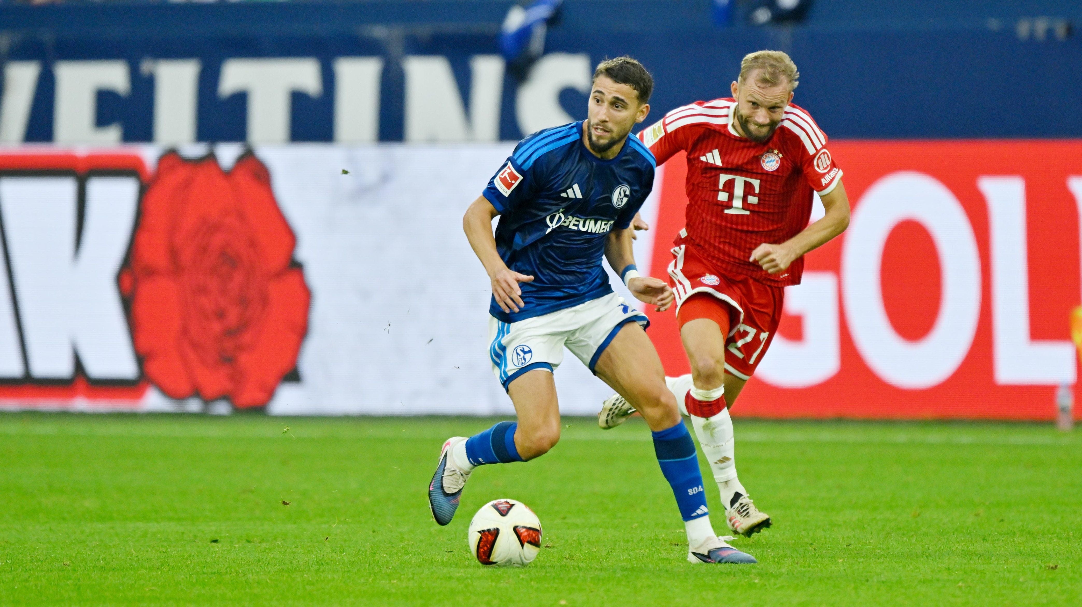 Ein Schalke-Spieler mit Ball wird von einem Bayern-Spieler während eines Fußballspiels verfolgt.