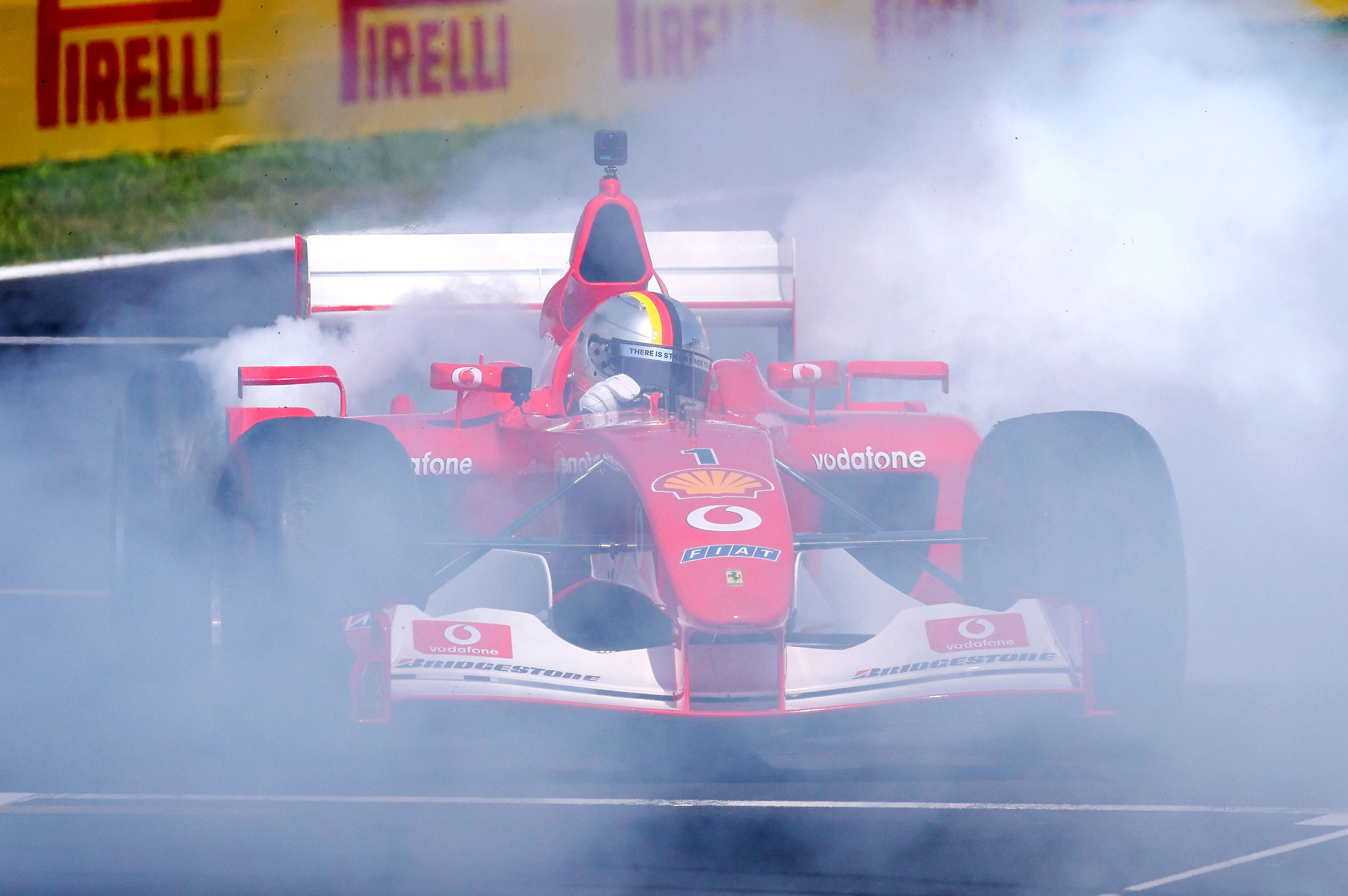 Ein rotes Ferrari-Formel-1-Auto macht Donuts und erzeugt dichten Reifenrauch auf der Strecke.