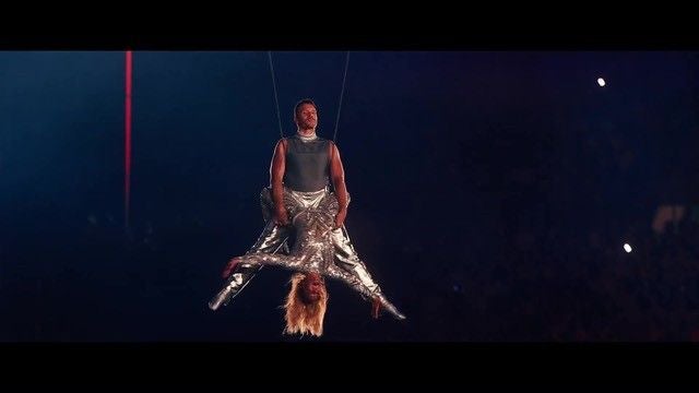 Zwei Artisten in silbernen Outfits führen eine Luftakrobatik-Nummer auf, einer hängt kopfüber.