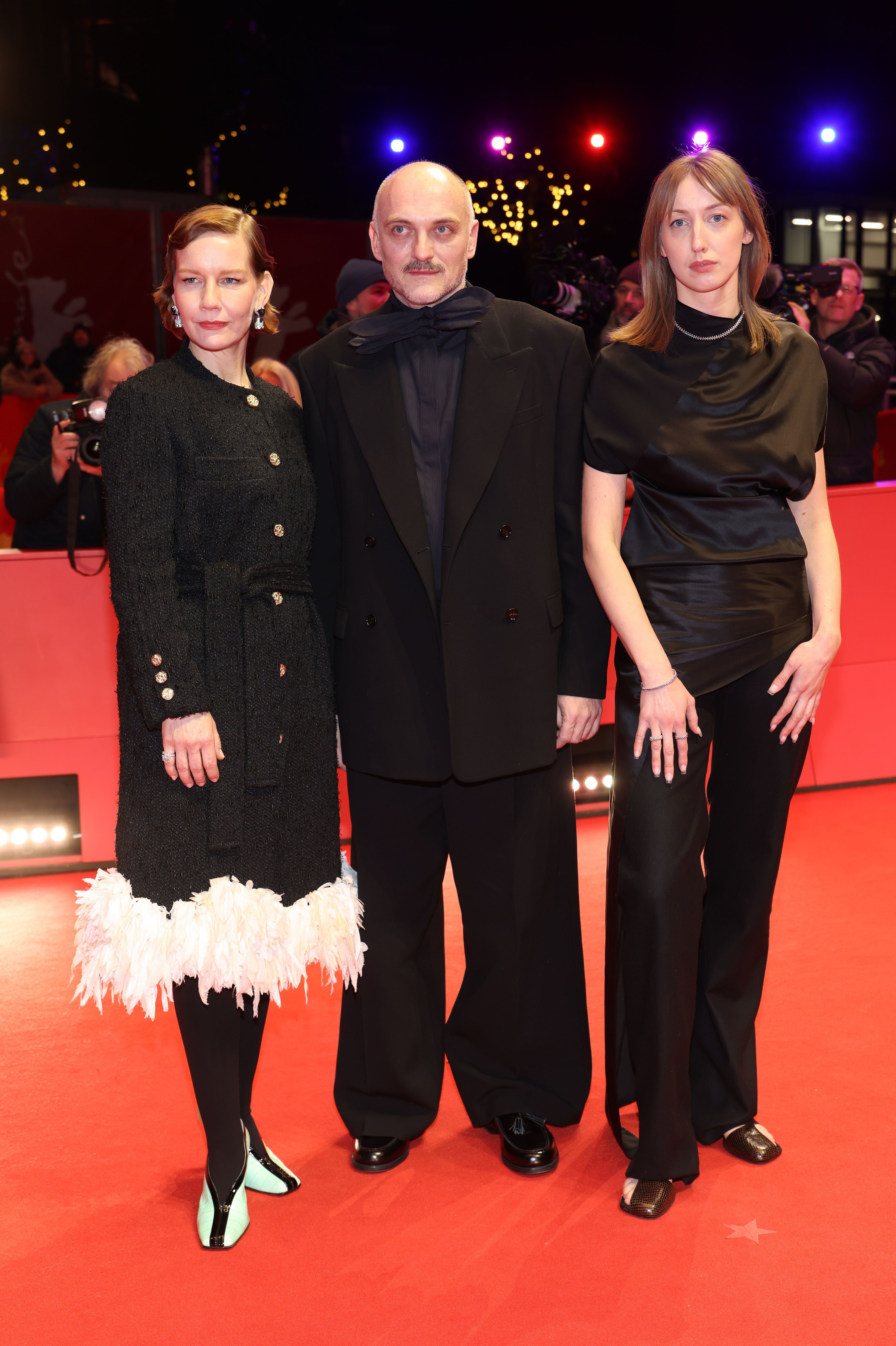 Drei elegant gekleidete Personen posieren gemeinsam auf dem roten Teppich bei einer Filmpremiere.