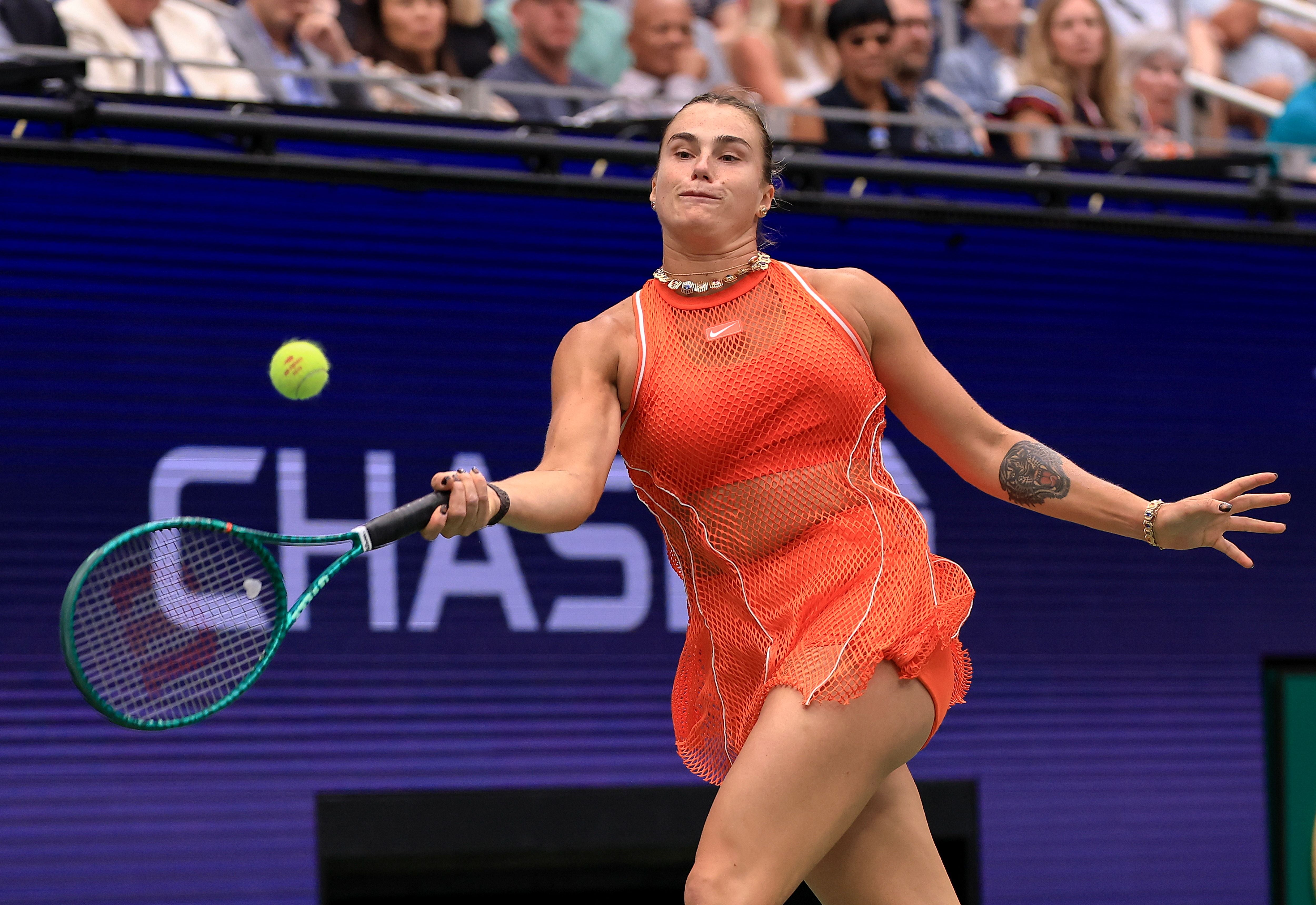 Die Tennisspielerin Aryna Sabalenka schlägt im orangen Outfit eine Vorhand auf dem Hartplatz.