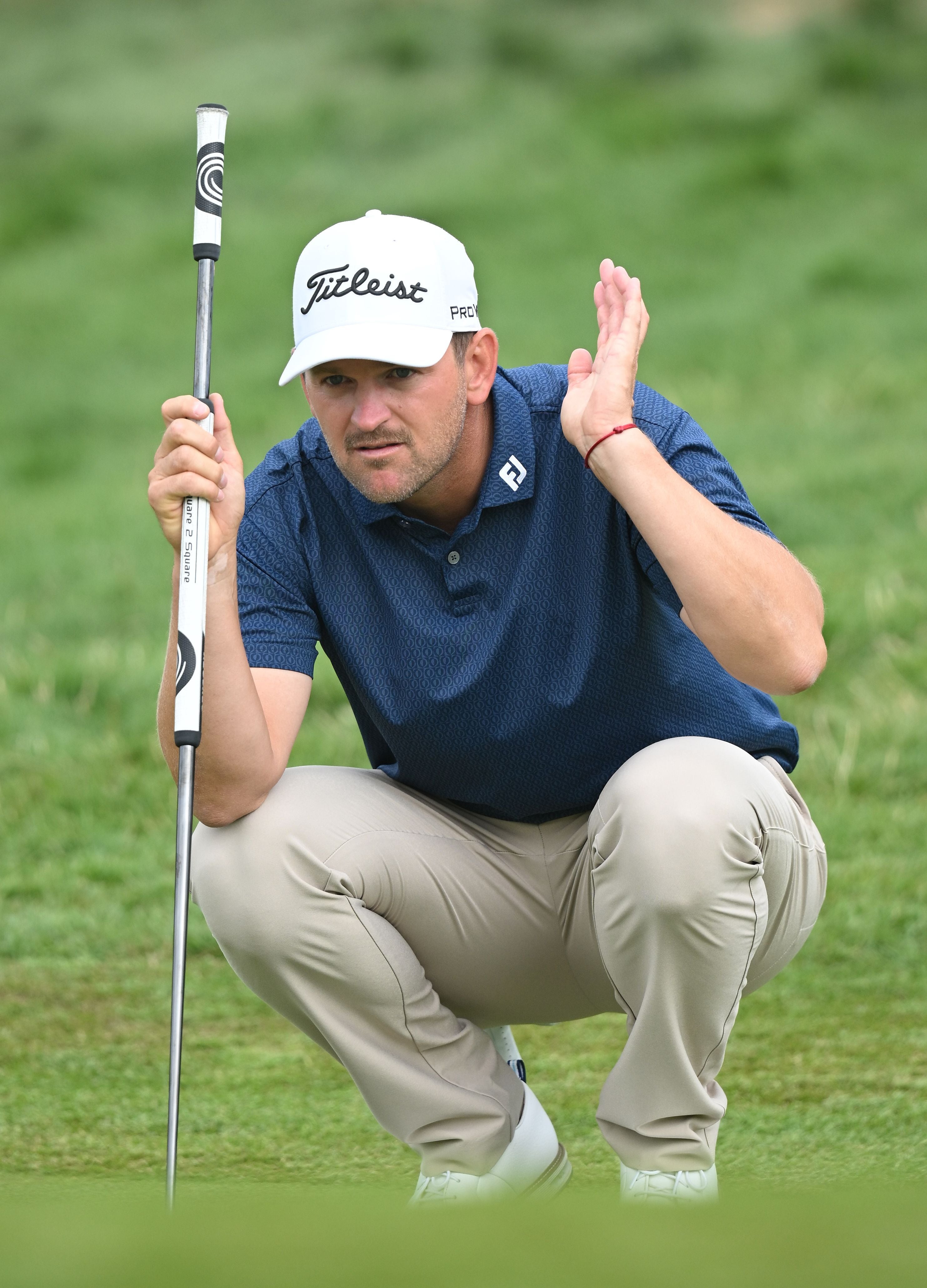 Golfprofi Bernd Wiesberger kniet im blauen Hemd auf dem Green und begutachtet mit erhobener Hand den Muldungsverlauf.