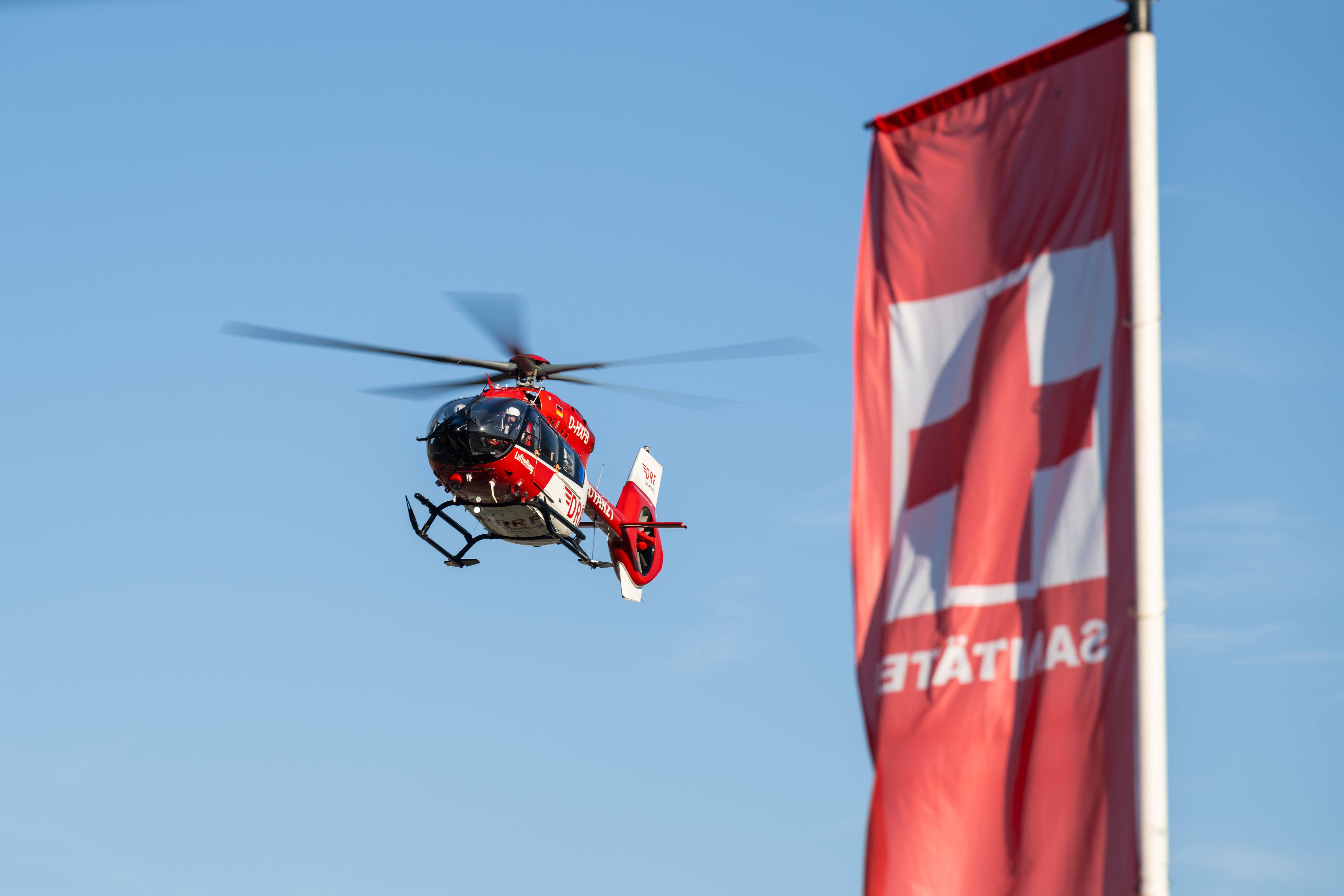Ein Rettungshubschrauber fliegt neben einer roten Rettungsflagge am Himmel über dem Festivalgelände.