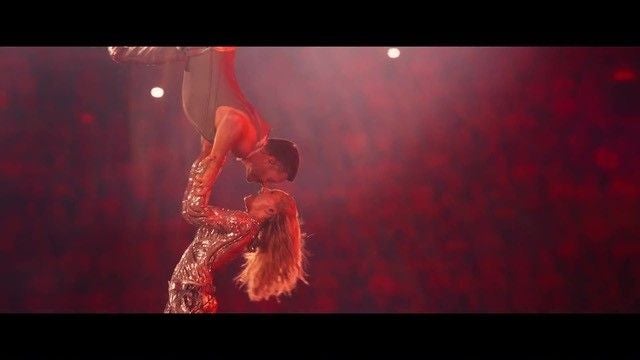 Akrobatin hält einen Mann kopfüber bei einer Bühnenperformance im roten Scheinwerferlicht.