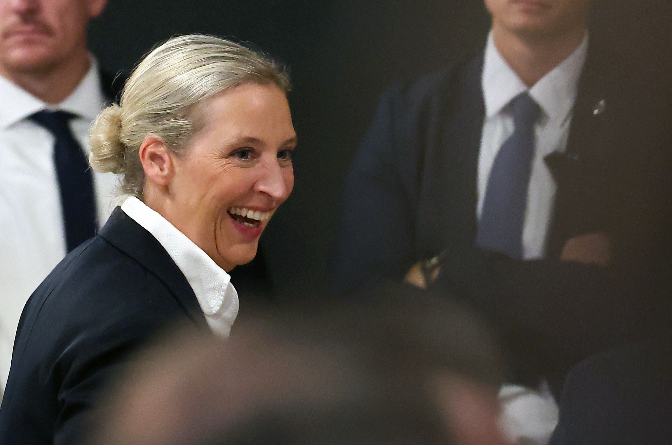 Eine lachende Frau in Anzugjacke bei einer Veranstaltung in Innenraumumgebung.