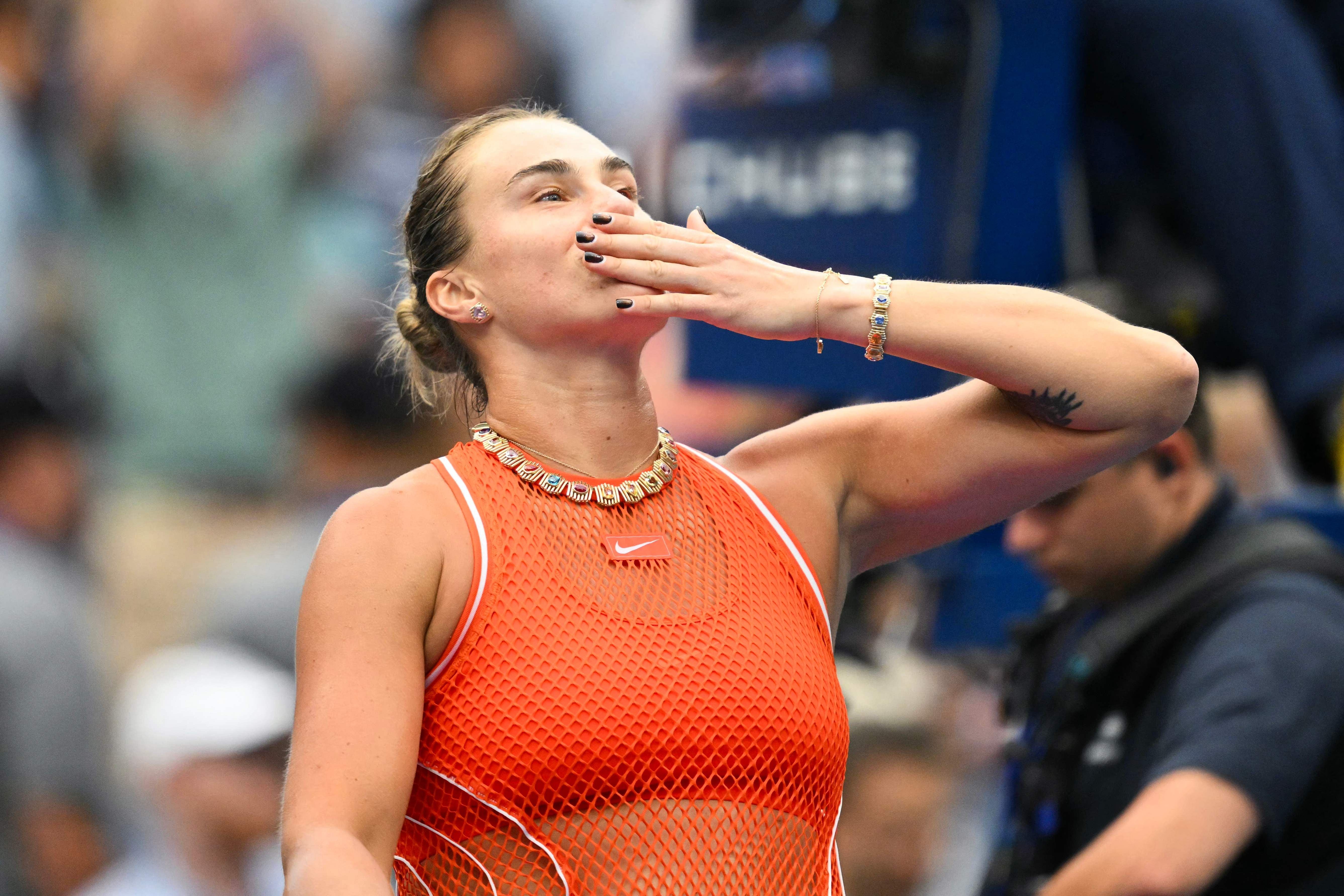 Tennisspielerin im orangefarbenen Outfit schickt dem Publikum einen Handkuss nach dem Spiel.