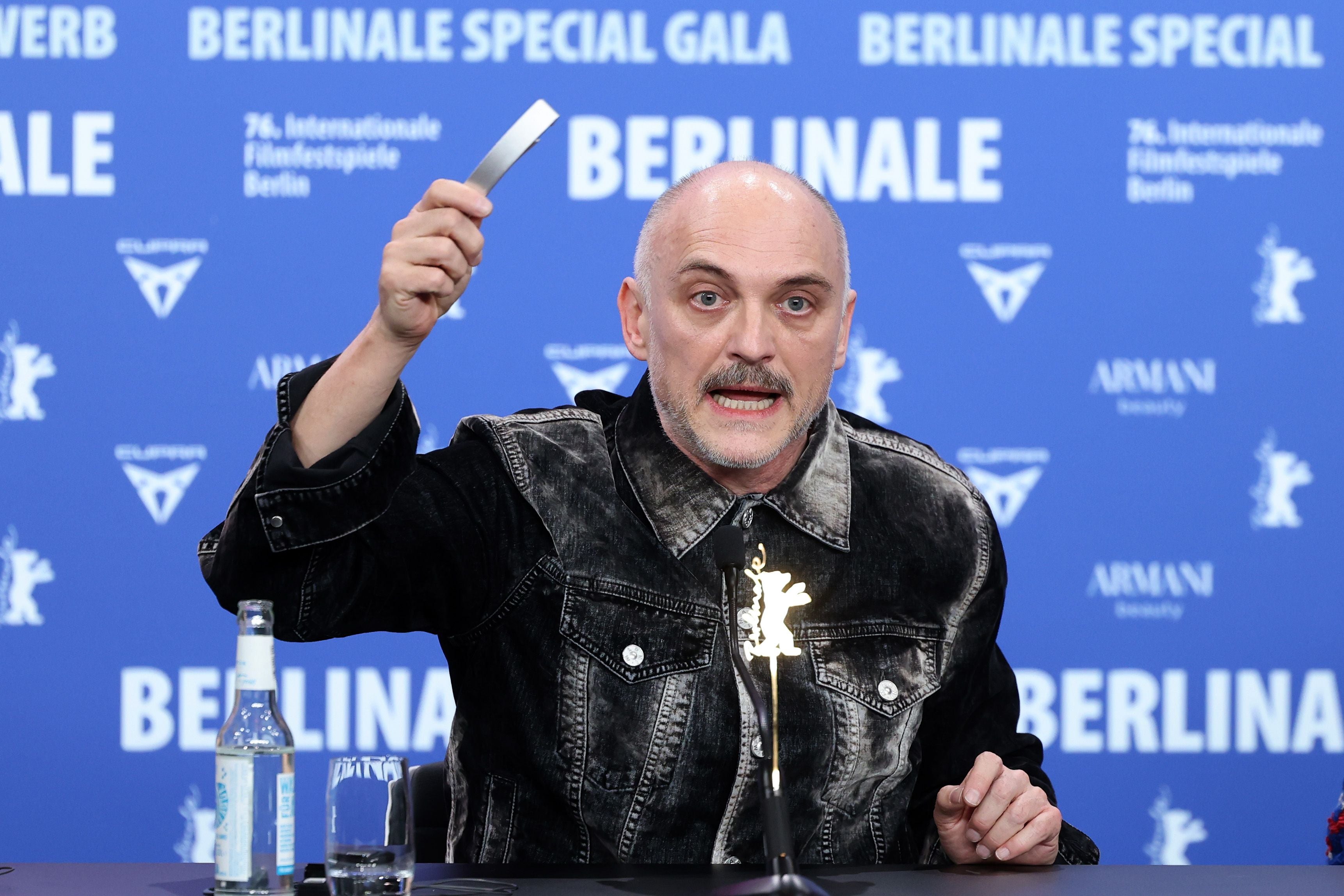 Ein Mann spricht auf einer Pressekonferenz der Berlinale und hält einen Gegenstand in die Luft.
