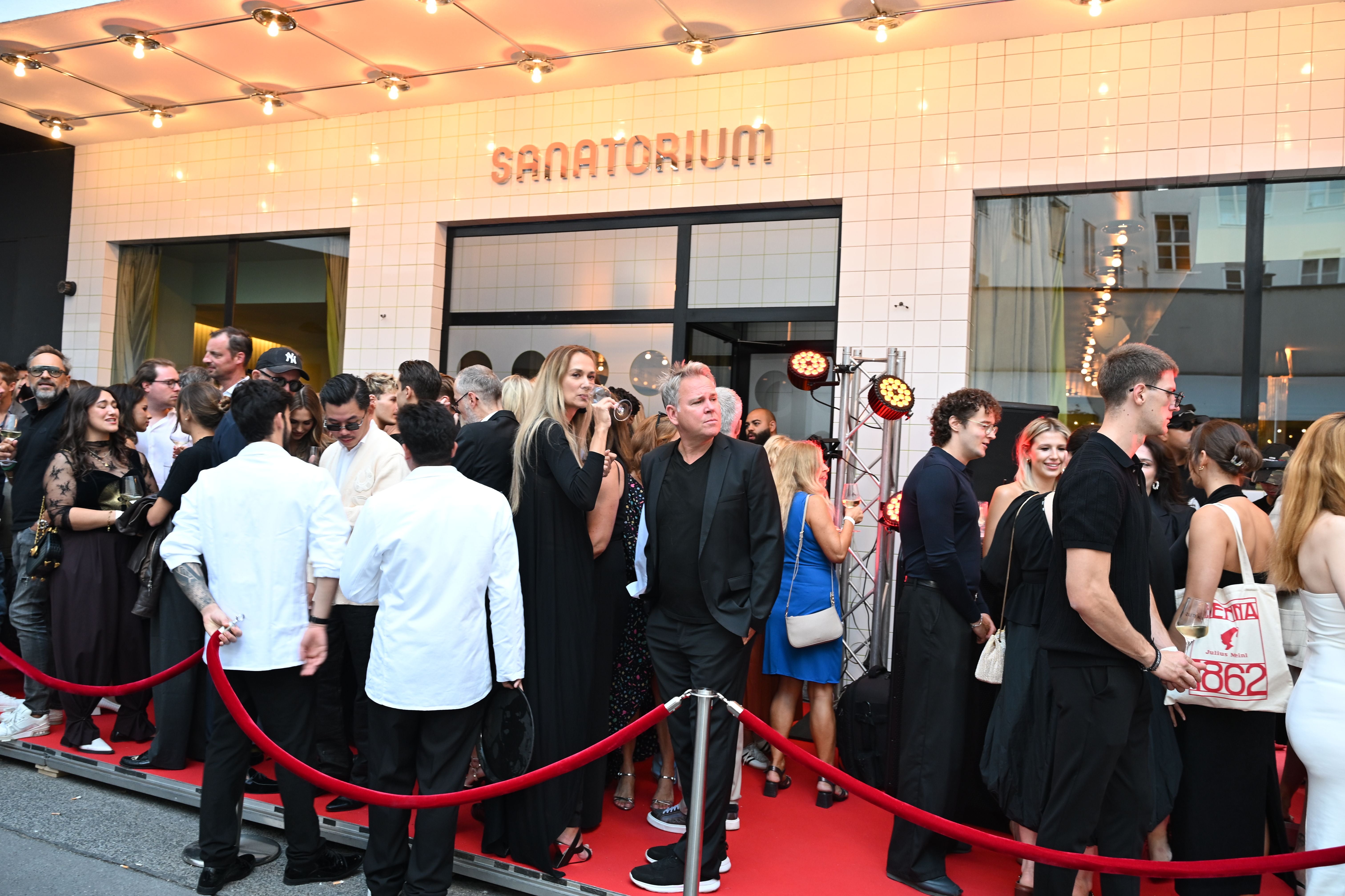 Viele elegant gekleidete Menschen stehen beim Sanatorium-Opening auf einem roten Teppich.