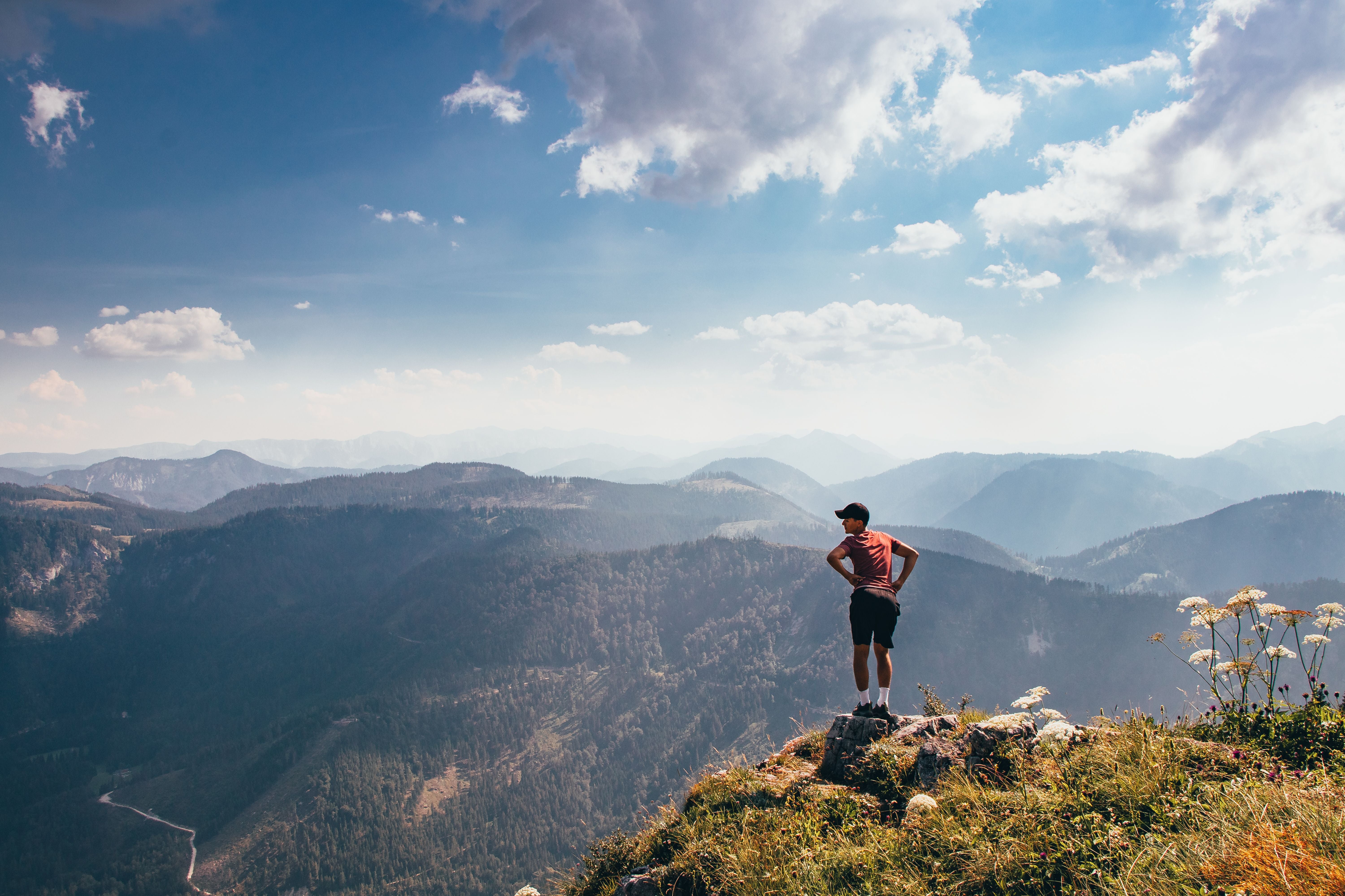 Ein junger Mann in Sportkleidung steht auf einem Felsen und blickt über bewaldete Berge.