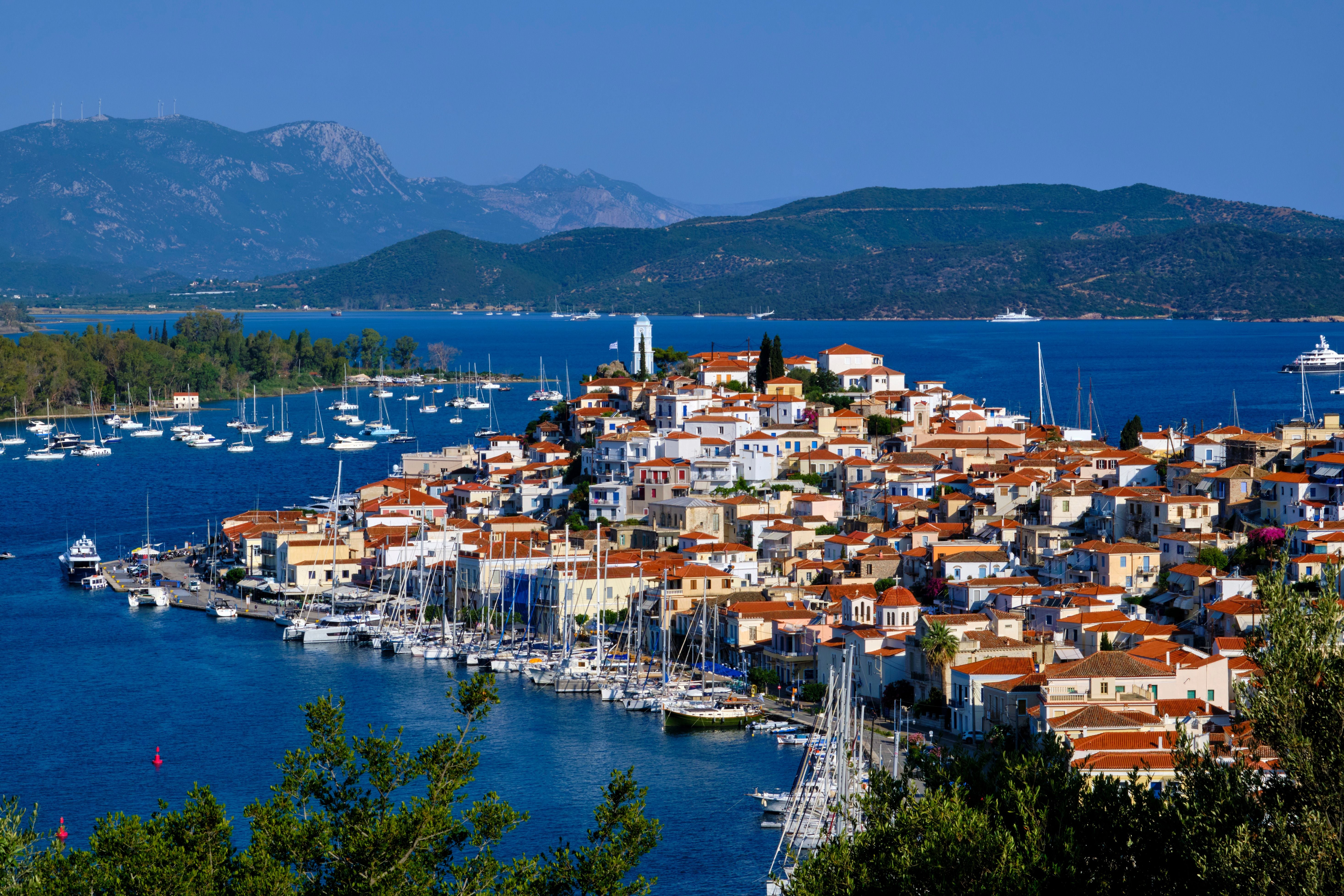 Blick auf Poros mit weißen Häusern, roten Dächern und Yachten am Hafen, umgeben vom Meer.