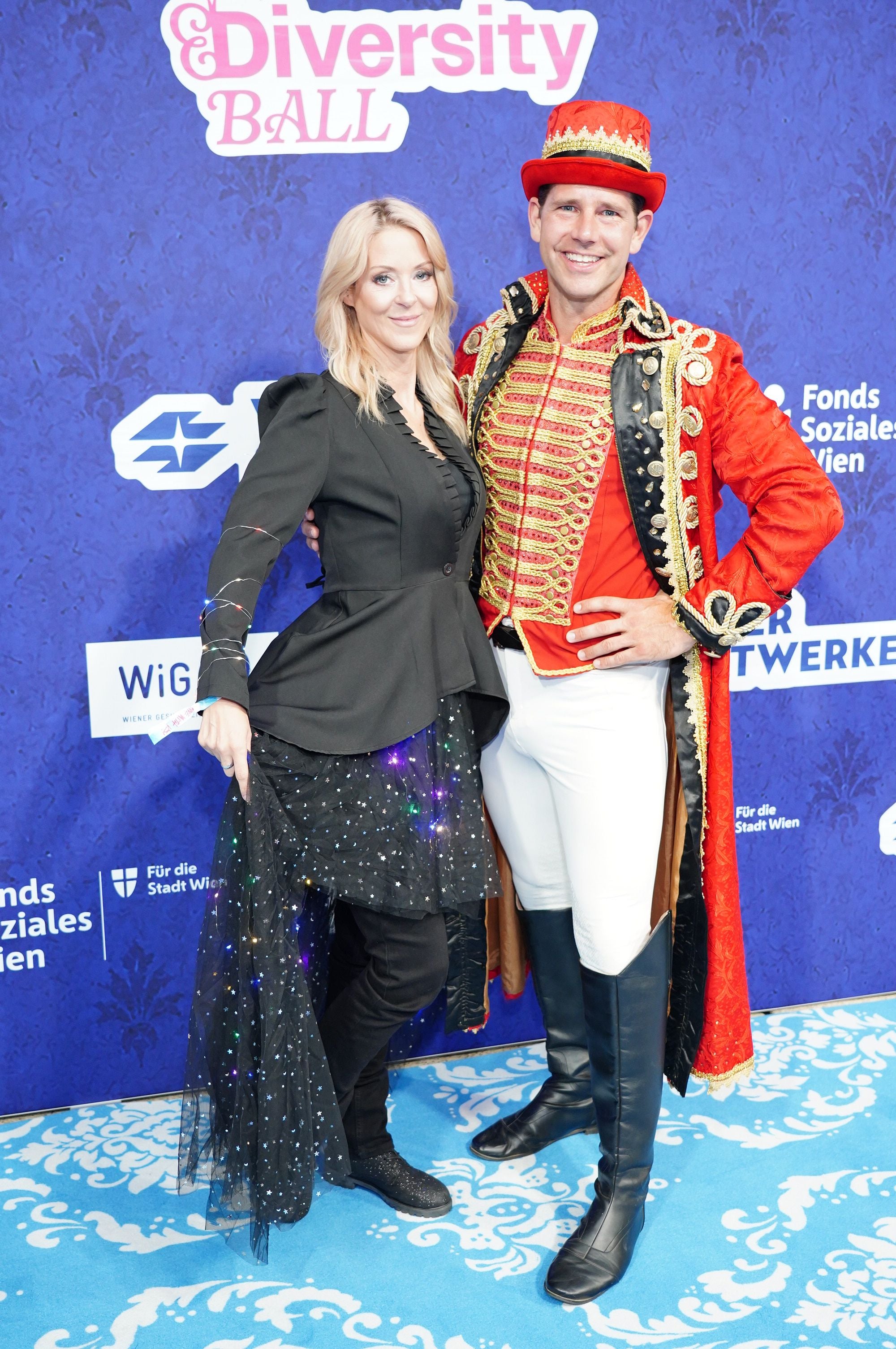 Zwei Personen in fantasievollen Outfits posieren beim Diversity Ball vor blauem Hintergrund.