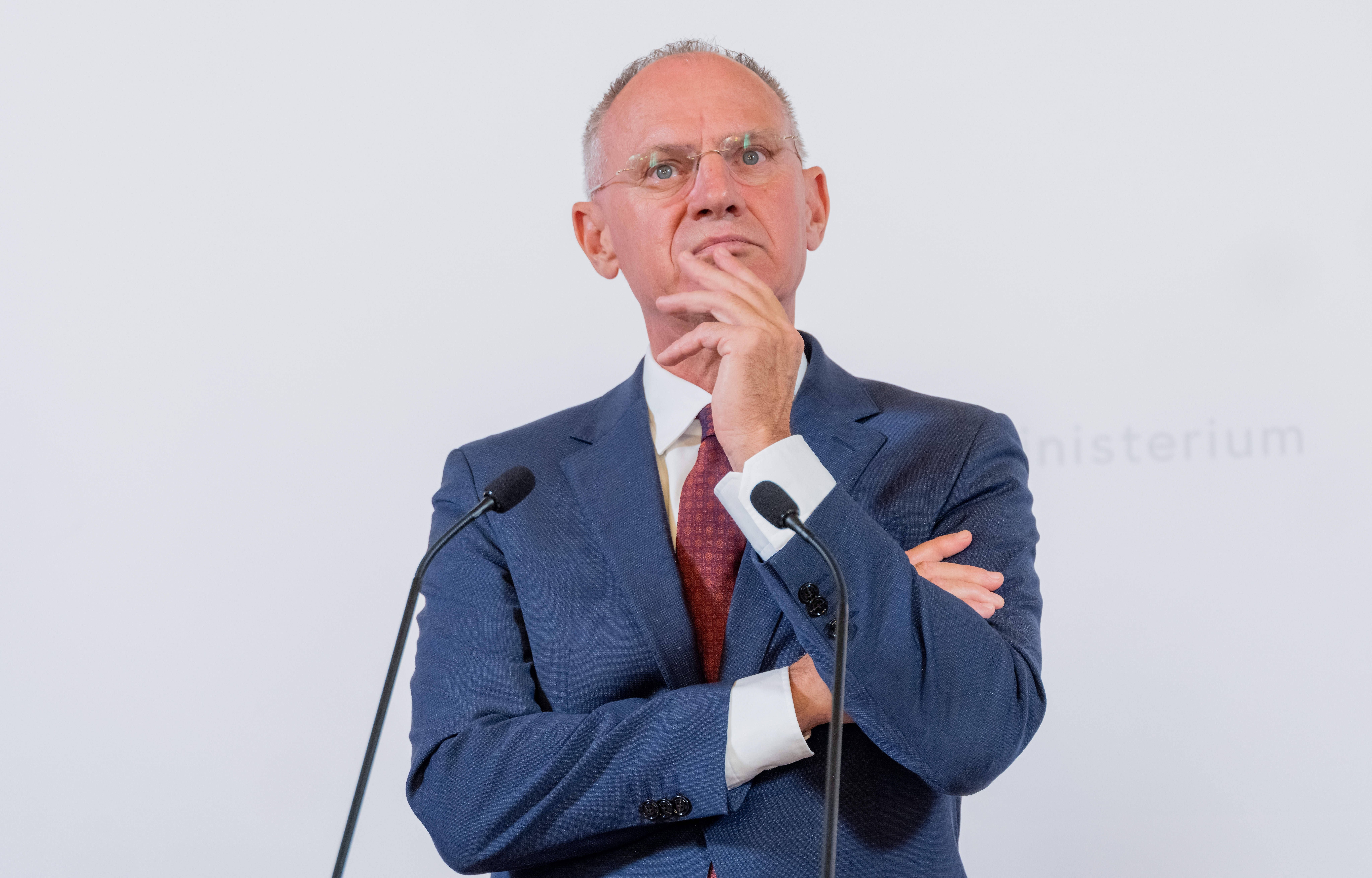 Mann im Anzug steht nachdenklich vor Mikrofonen bei einer Pressekonferenz.