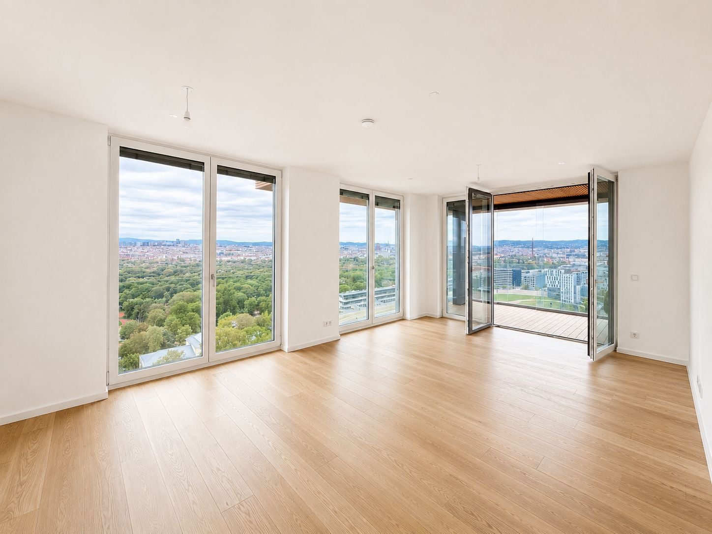 Helles, leeres Zimmer mit Holzboden und Panoramafenstern mit Blick auf Stadt und Natur.