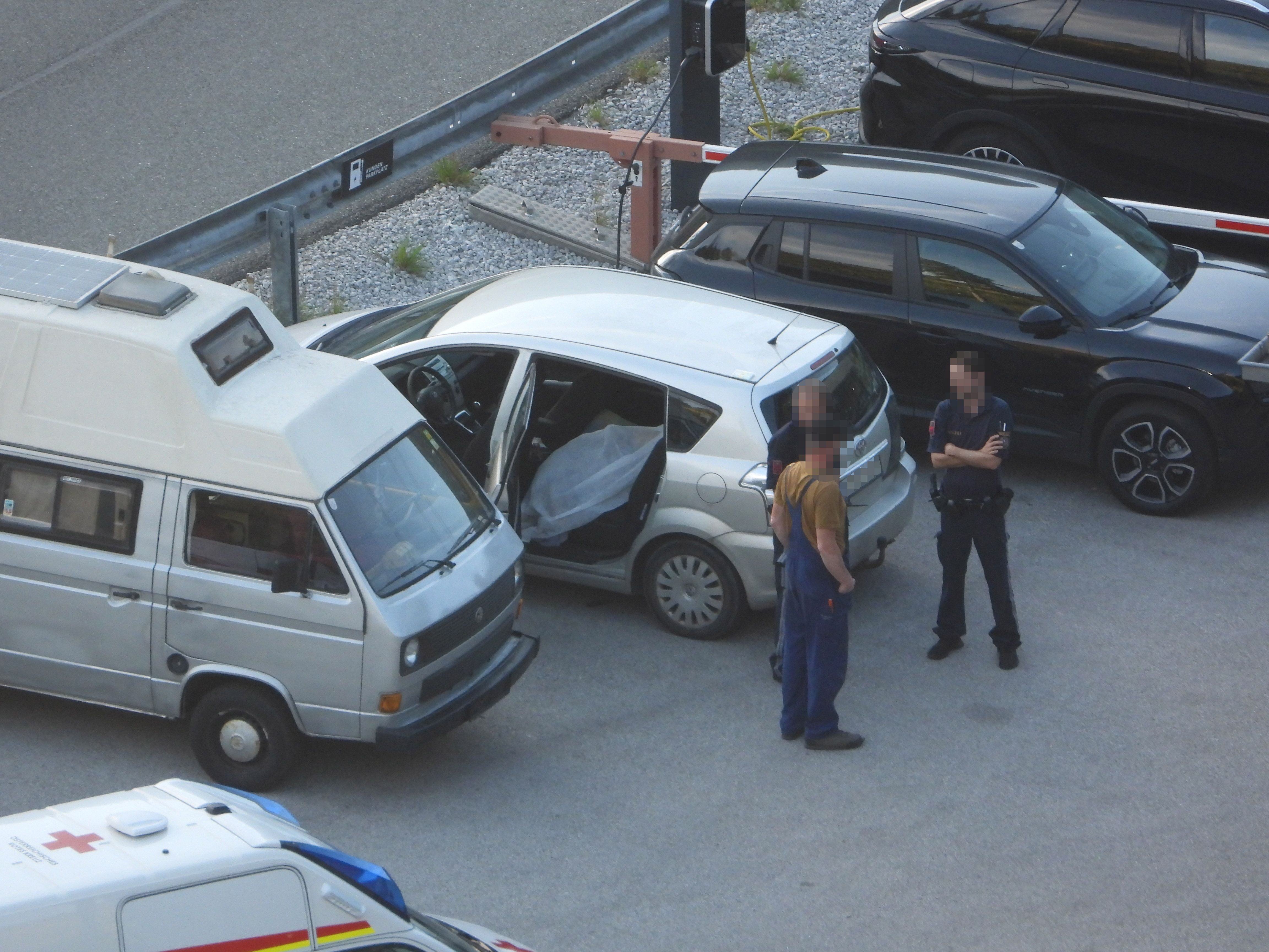 Polizist und Mann stehen neben geöffnetem Auto, Rettungswagen und Transporter im Hintergrund.