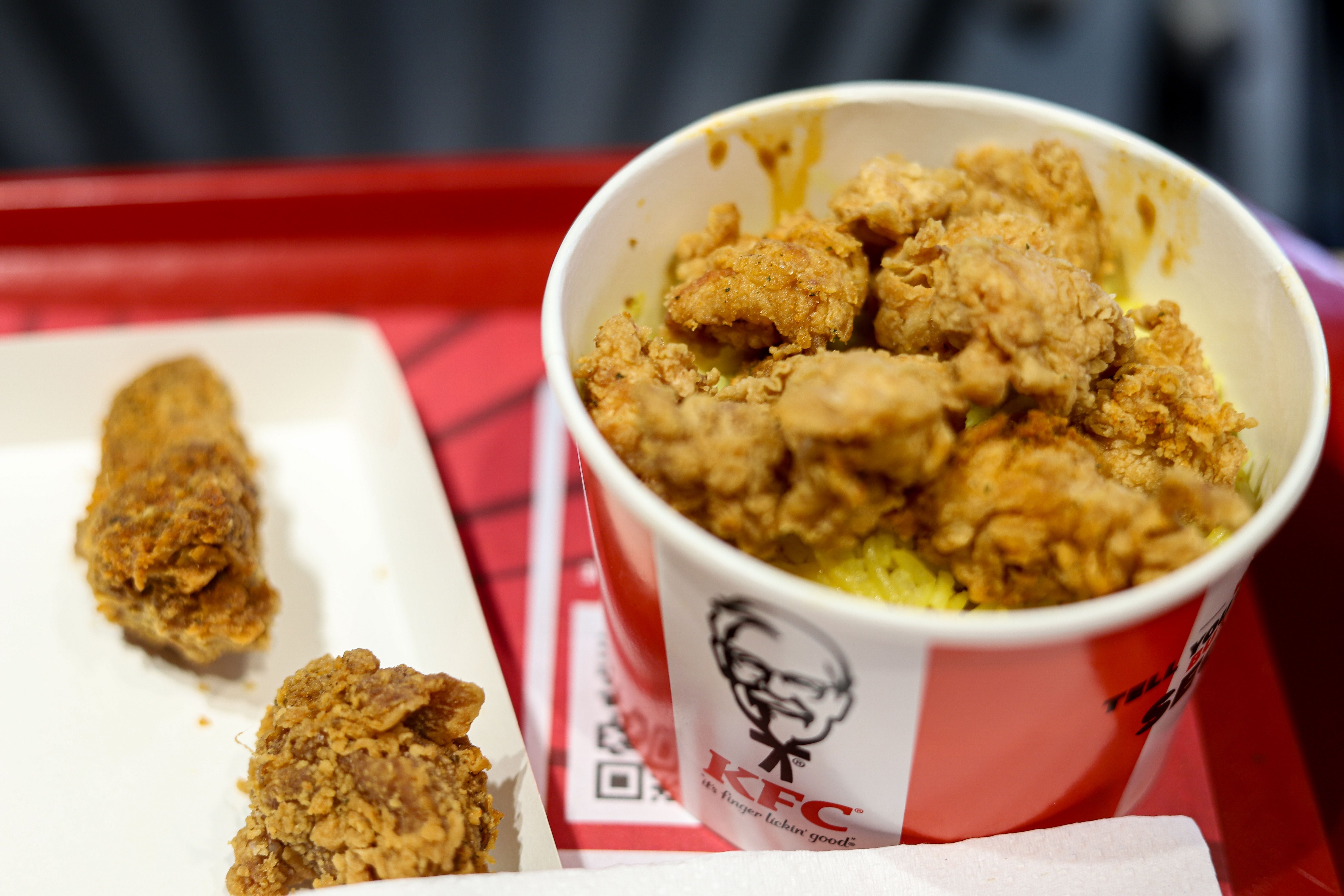 KFC-Hähnchenreis-Eimer und frittiertes Hähnchenstück auf einem Tablett in einem Restaurant.