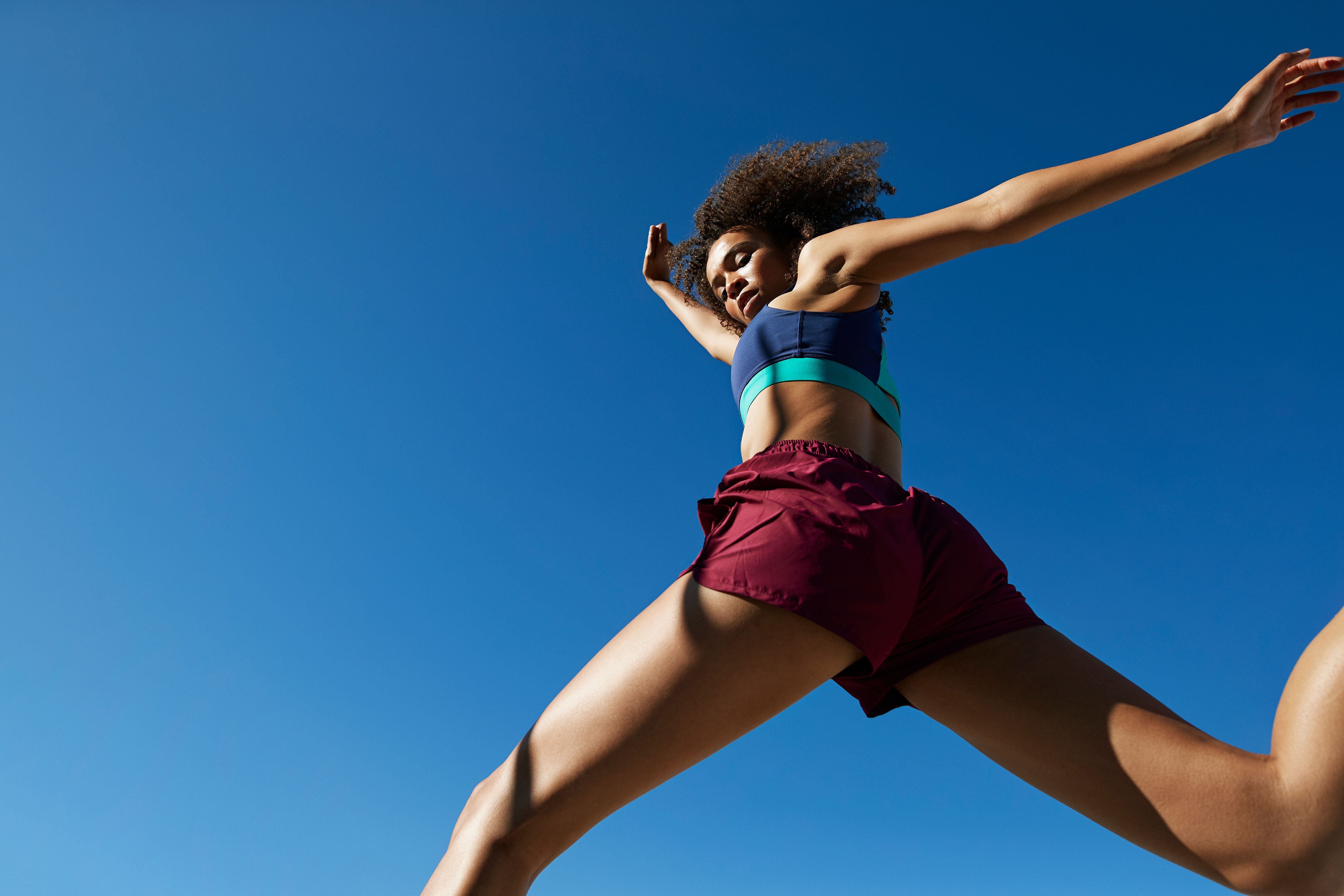 Sportlerin mit lockigem Haar springt vor blauem Himmel an einem sonnigen Tag.