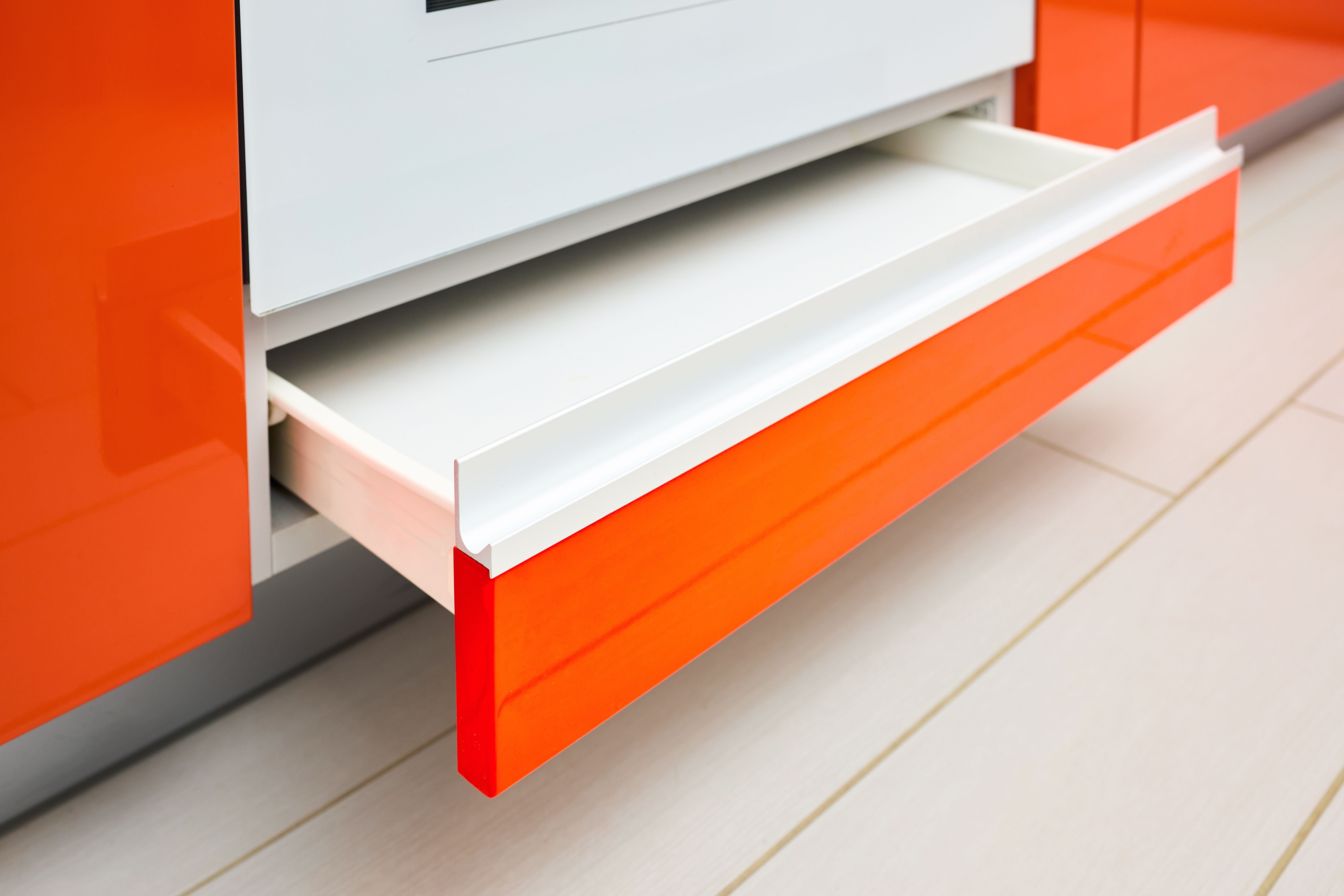 Offene, orangefarbene Küchenschublade unter einem Backofen auf hellen Fliesenboden.