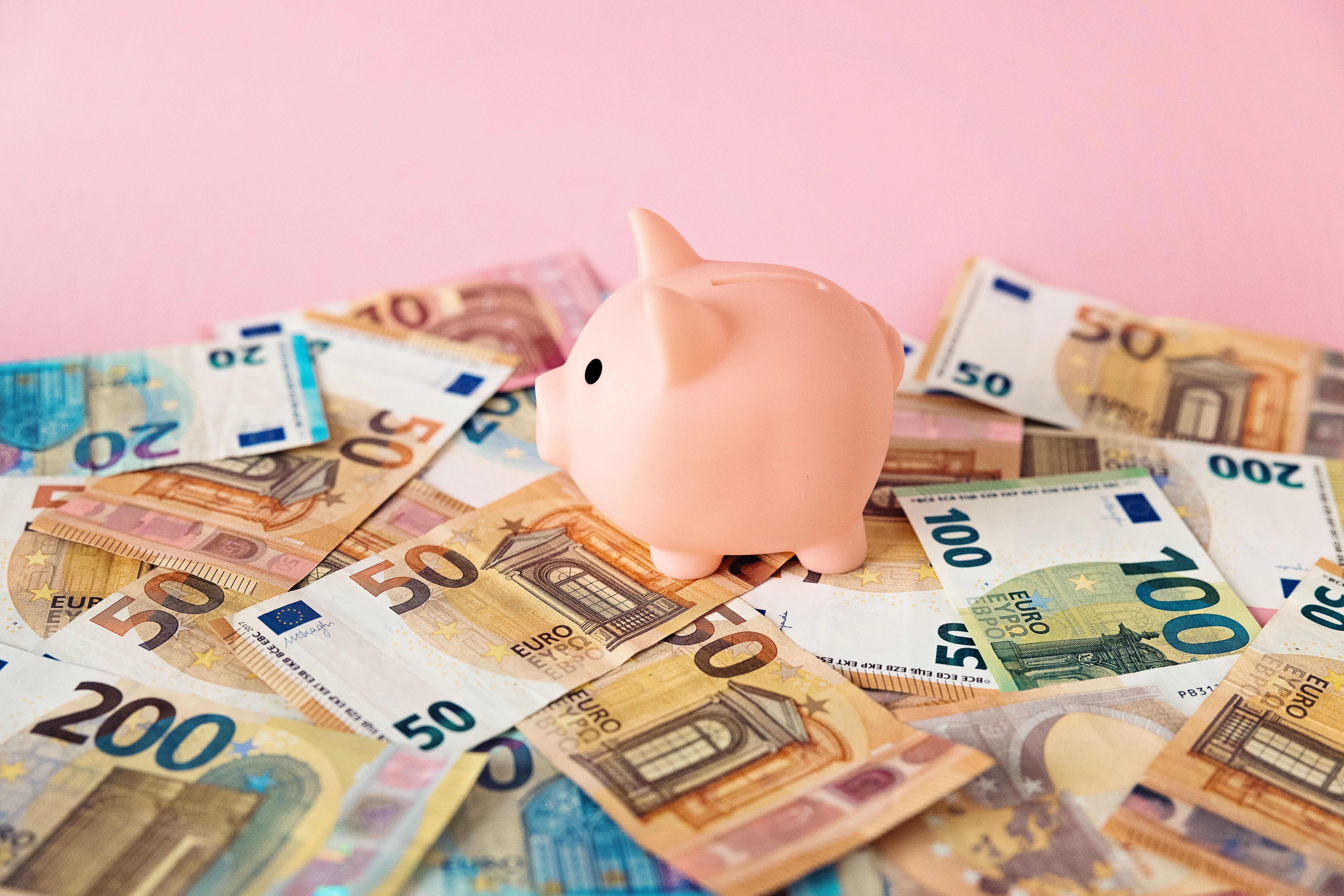 Ein rosa Sparschwein steht auf vielen Euro-Geldscheinen vor einem rosa Hintergrund.