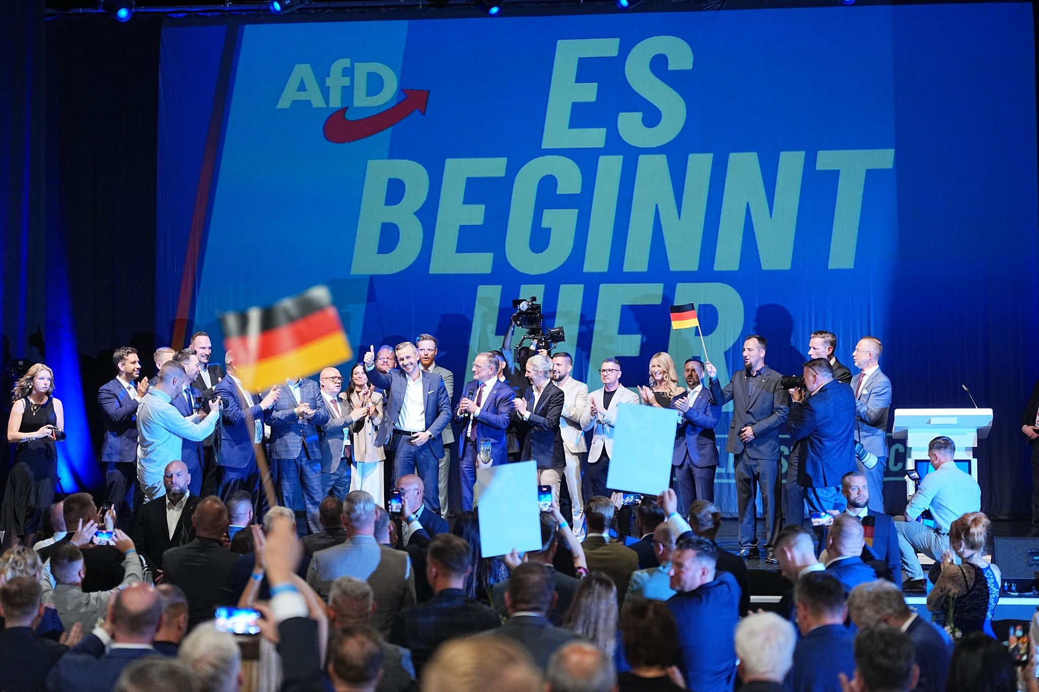 Menschen feiern auf einer AfD-Wahlparty in Magdeburg vor der Bühne mit dem Schriftzug "Es beginnt hier".