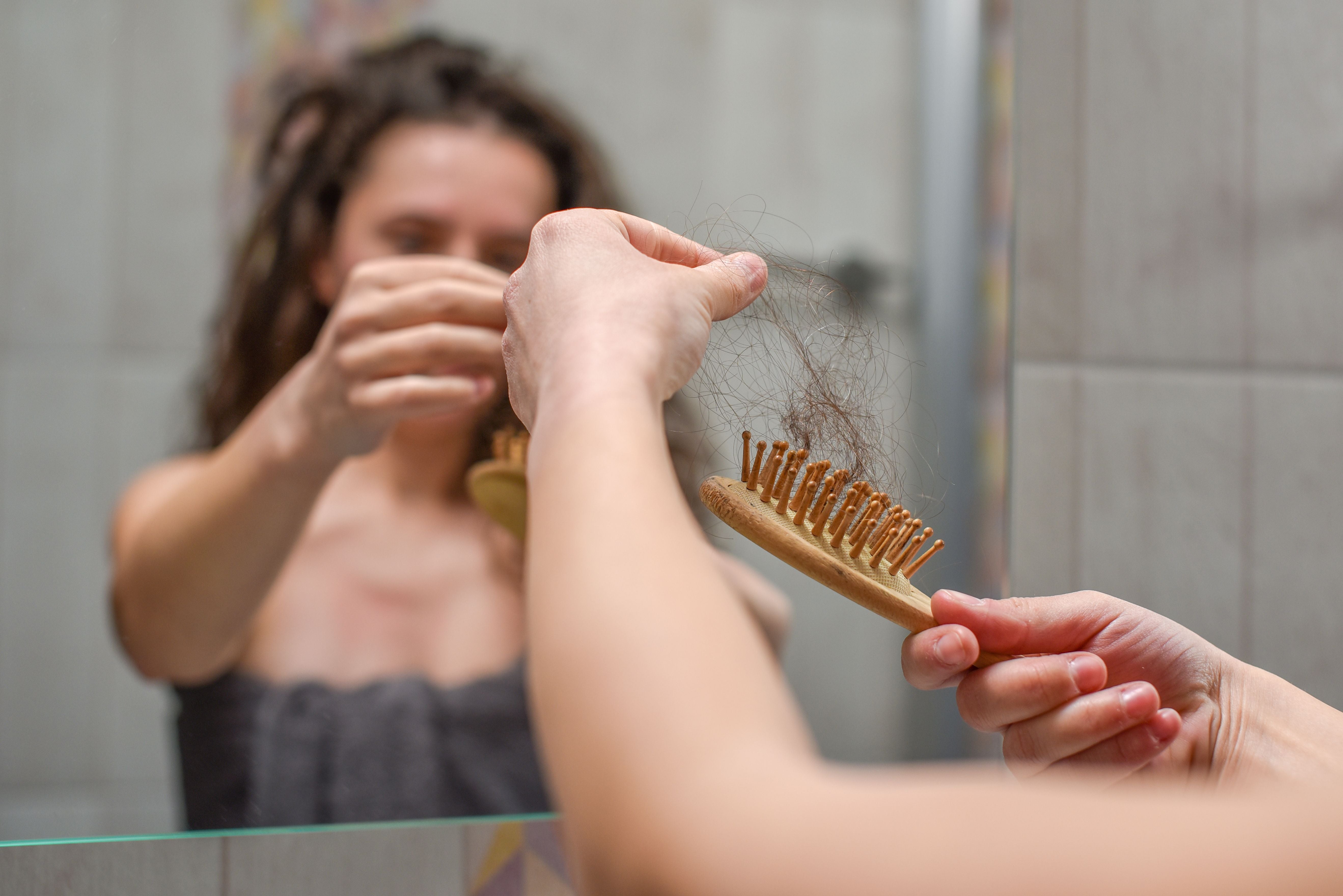 Frau betrachtet im Bad eine Bürste mit ausgefallenen Haaren, Thema Haarausfall.