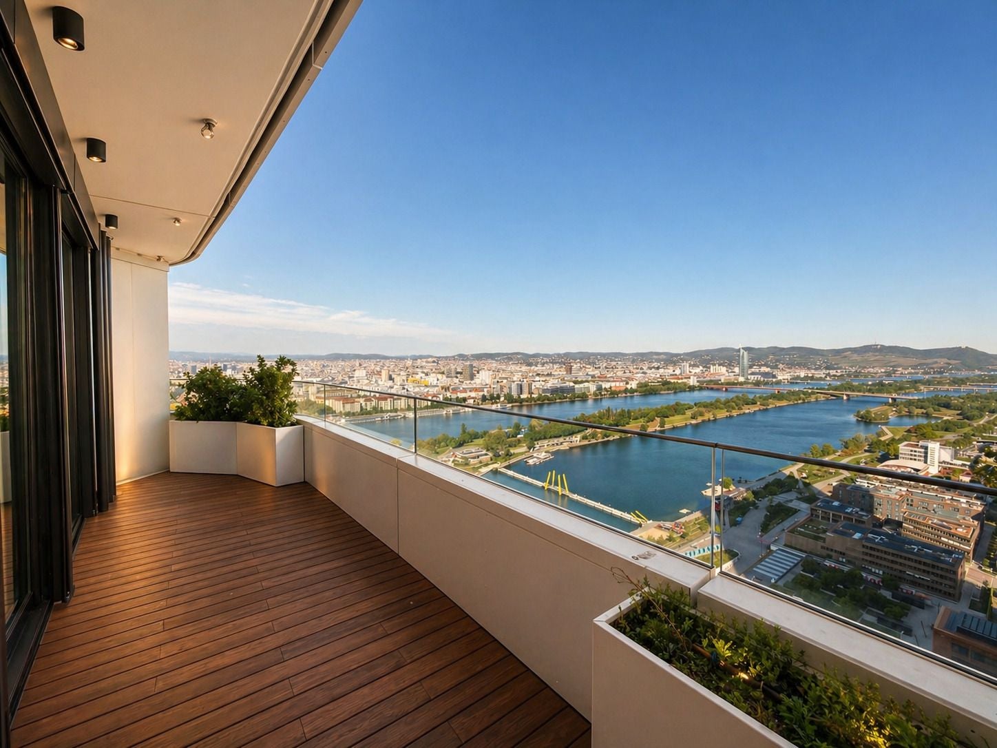 Großer Balkon mit Holzboden, Glasgeländer und Blick über Fluss, Stadt und grüne Landschaft.
