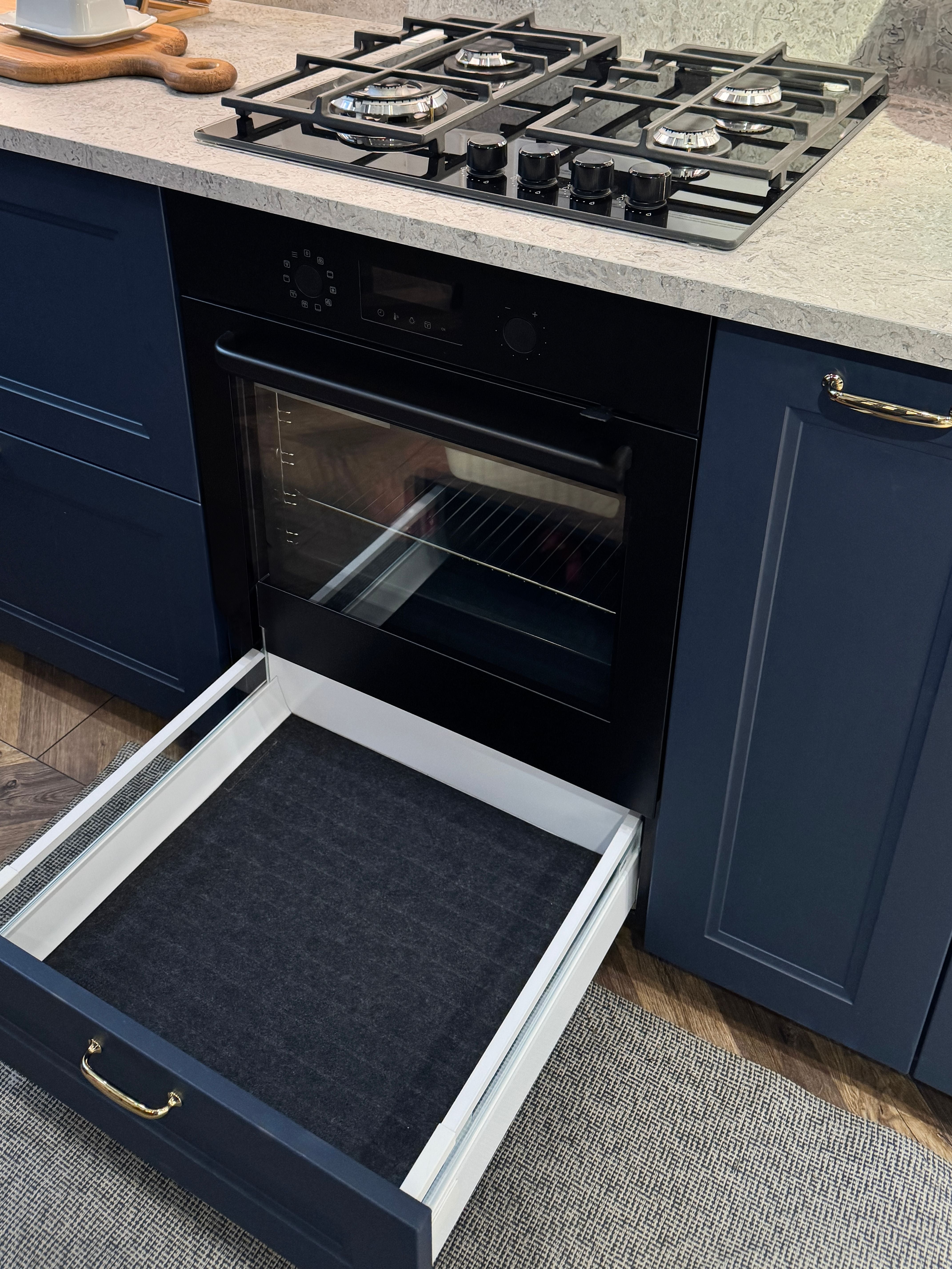 Moderner Backofen mit offener Unter-Schublade in einer eleganten Küche mit Gasherd und blauen Schränken.