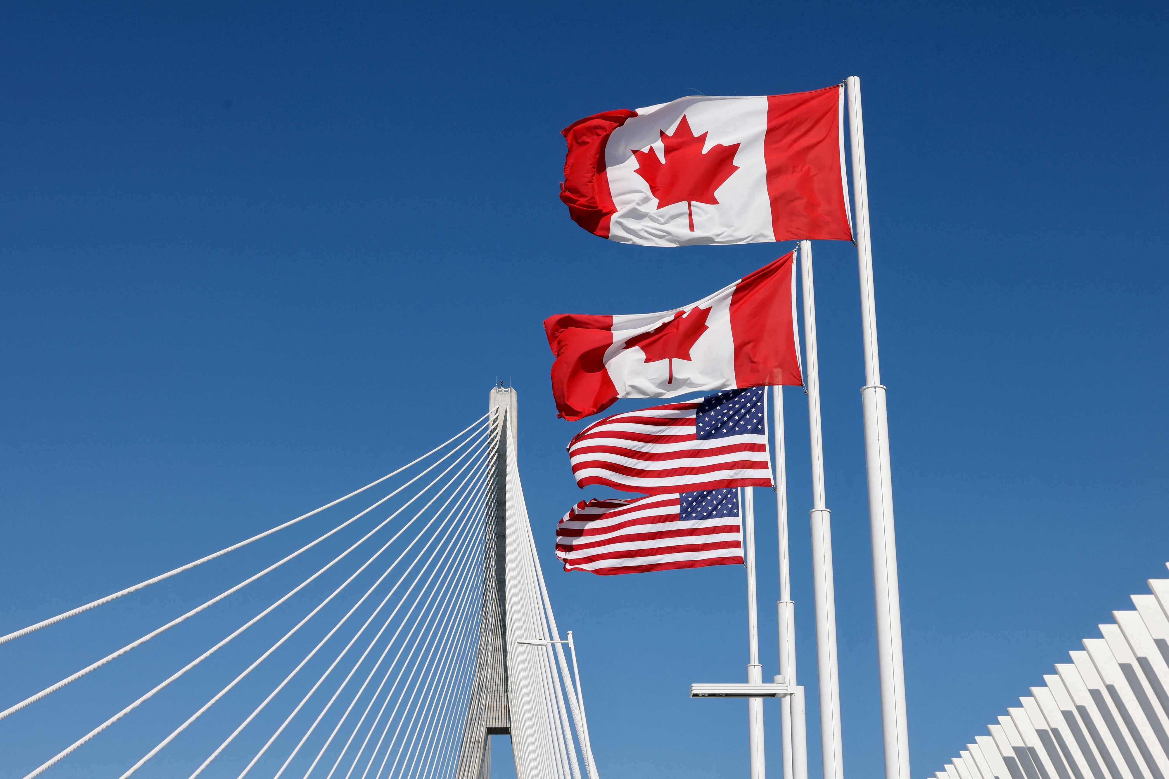 Kanadische und US-amerikanische Flaggen wehen vor einer modernen Schrägseilbrücke im Sonnenschein.