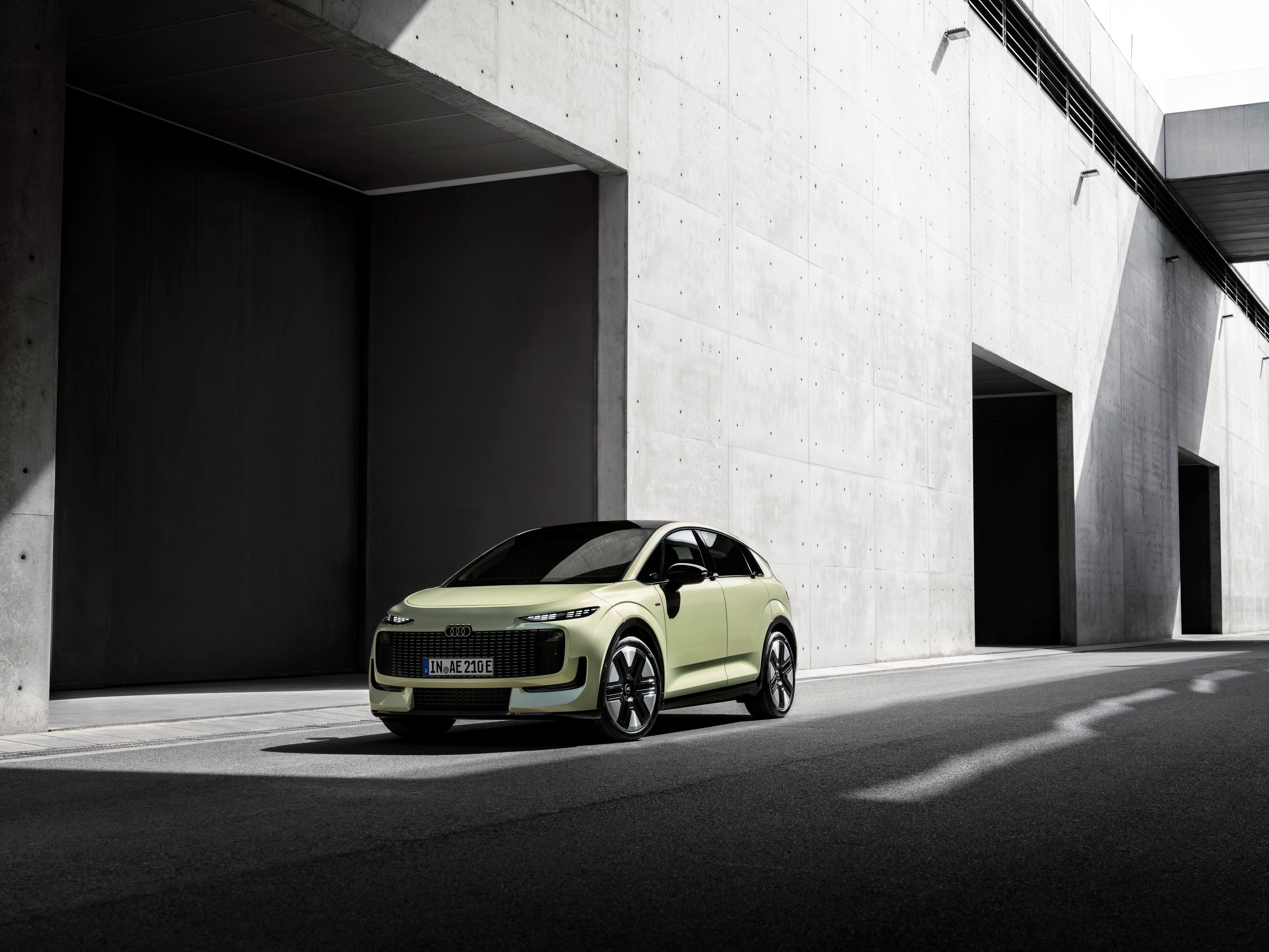 Ein pistaziengrüner Audi steht vor einer modernen Betonwand im Schatten.