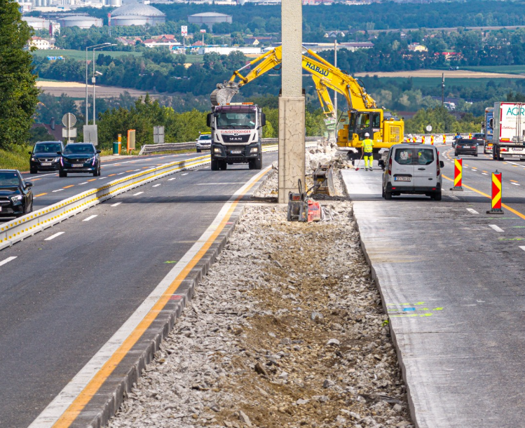 Straßenbauarbeiten auf einer Autobahn mit Bagger, LKW und abgesperrten Fahrspuren.