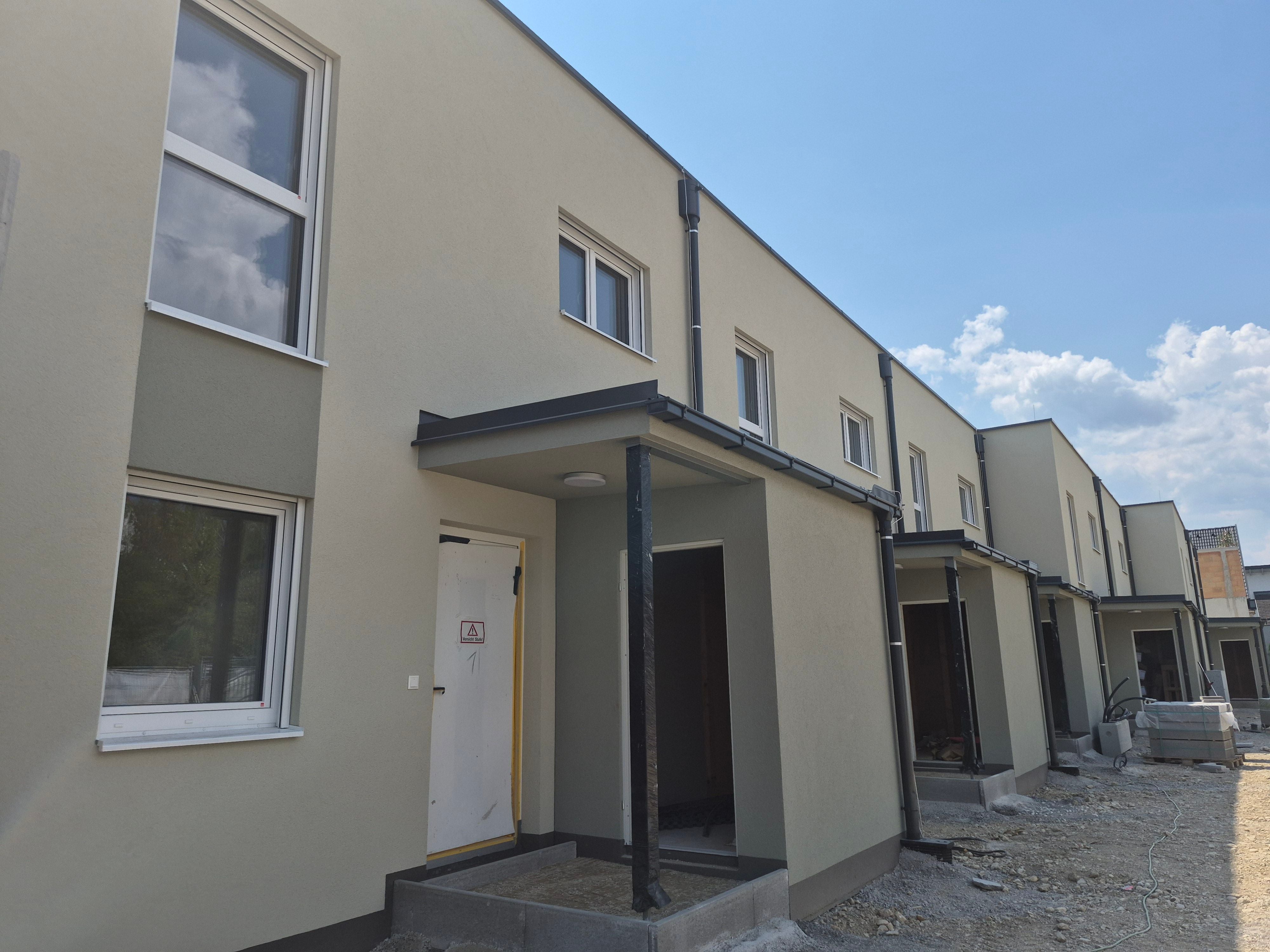 Reihenhäuser im Bau mit beigem Putz und Eingangsbereichen, Baustelle im Vordergrund.