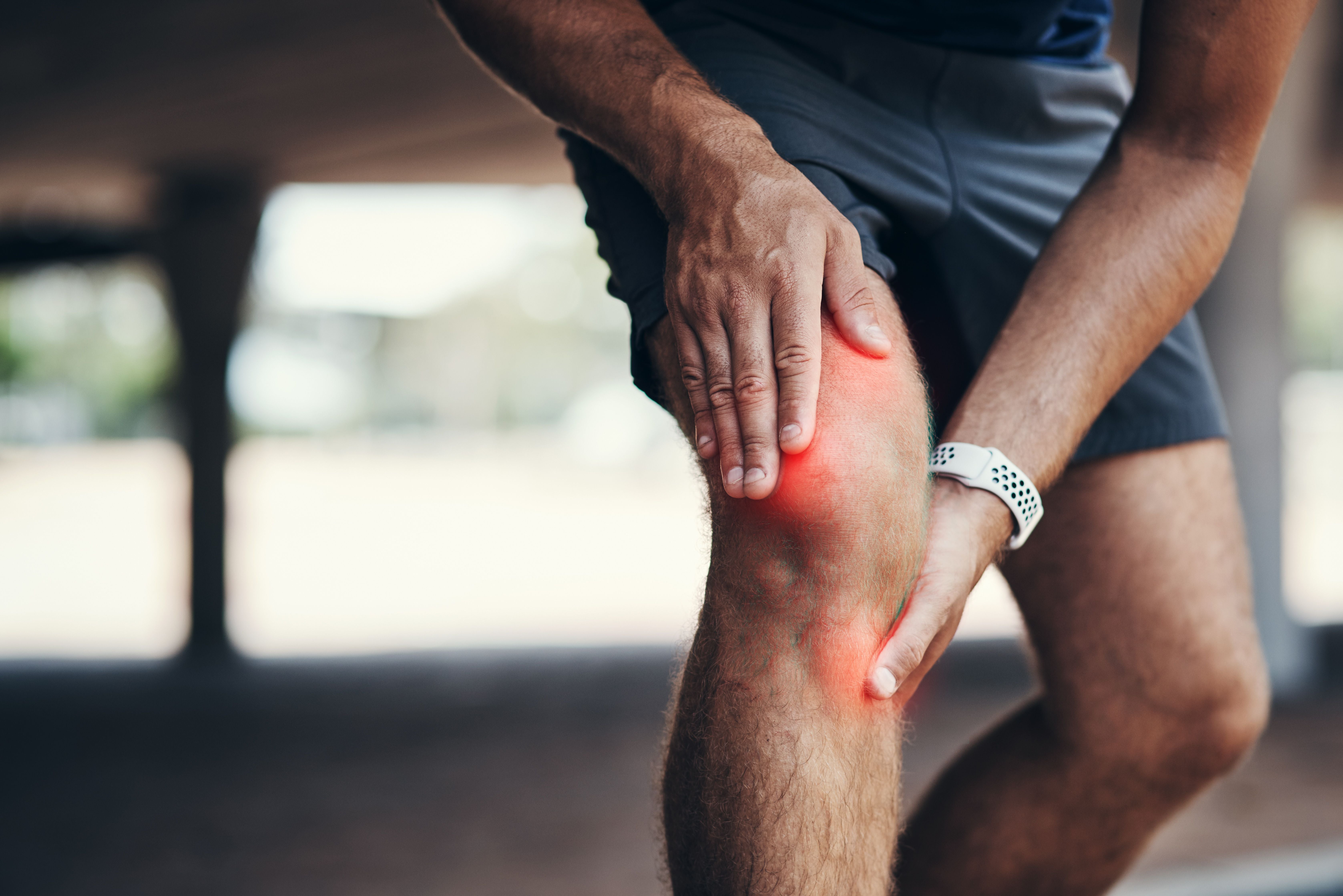Mann hält sich beim Sport im Freien schmerzhaft das Knie, das rot hervorgehoben ist.