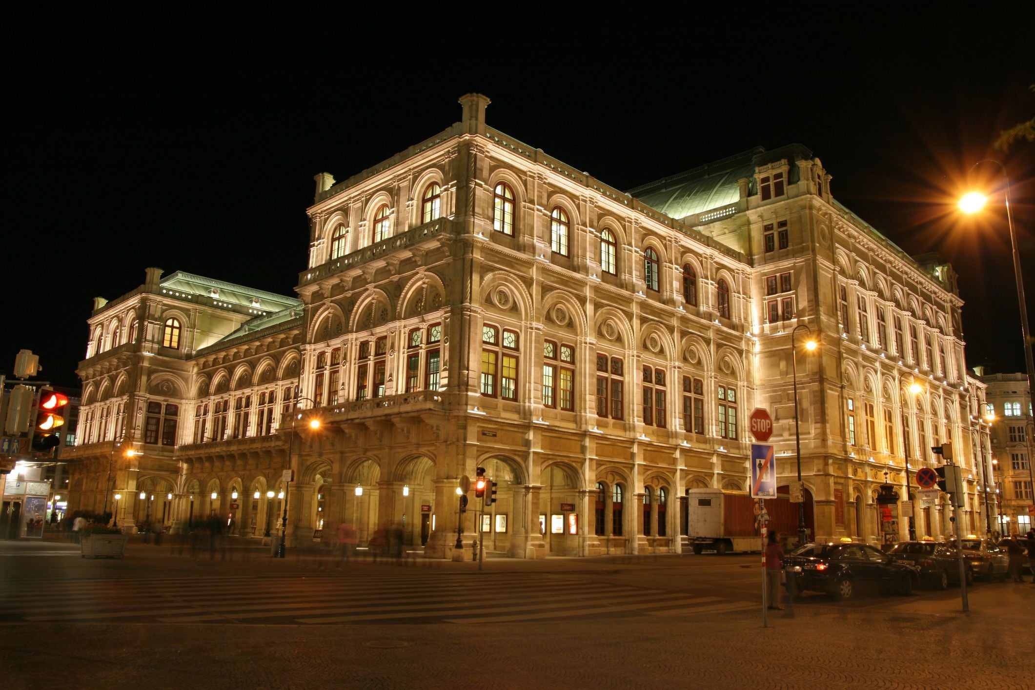 Die Wiener Staatsoper ist nachts eindrucksvoll beleuchtet, Autos parken davor.
