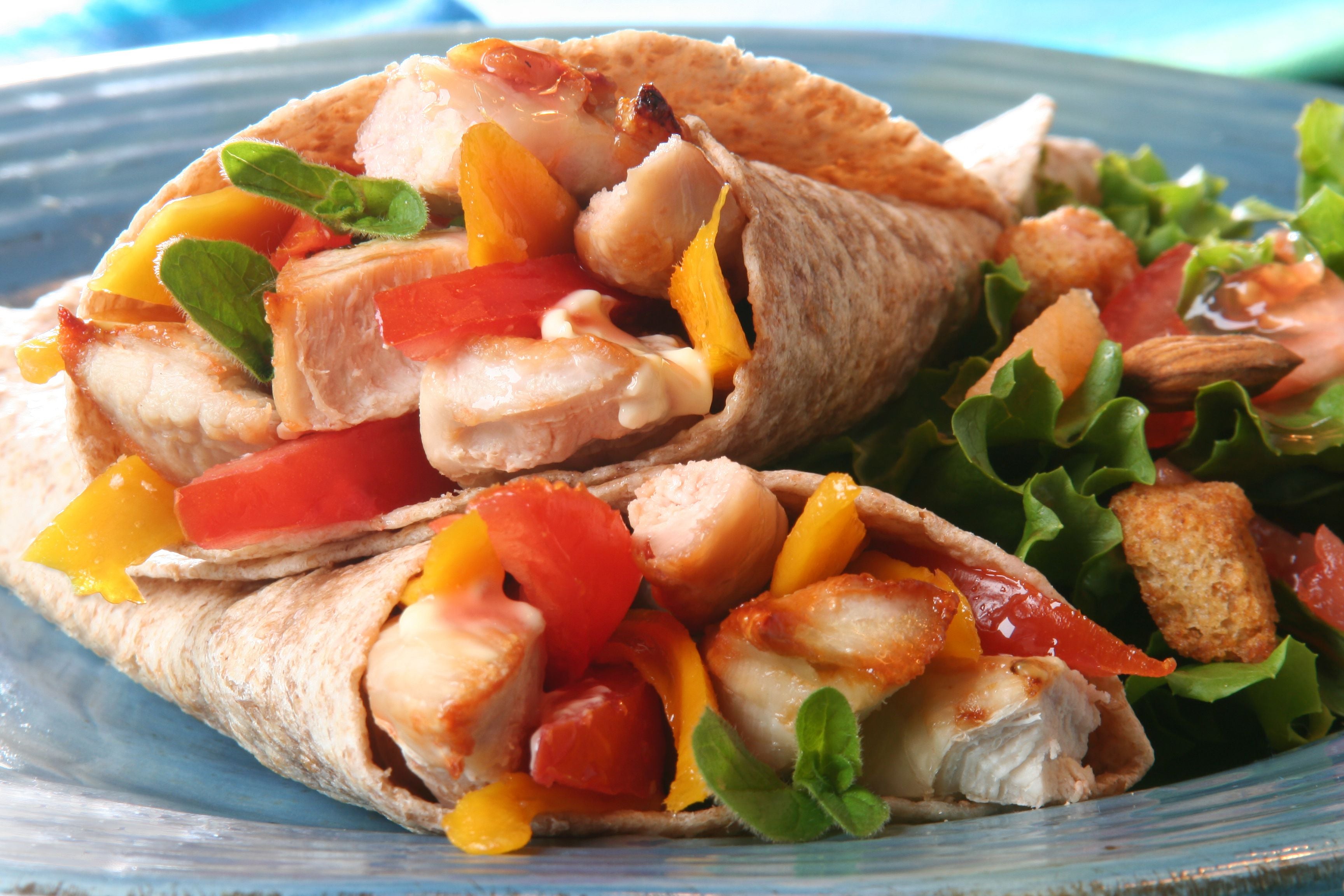 Zwei Hähnchen-Fajitas mit Paprika und Salat auf einem Teller, daneben ein grüner Beilagensalat.