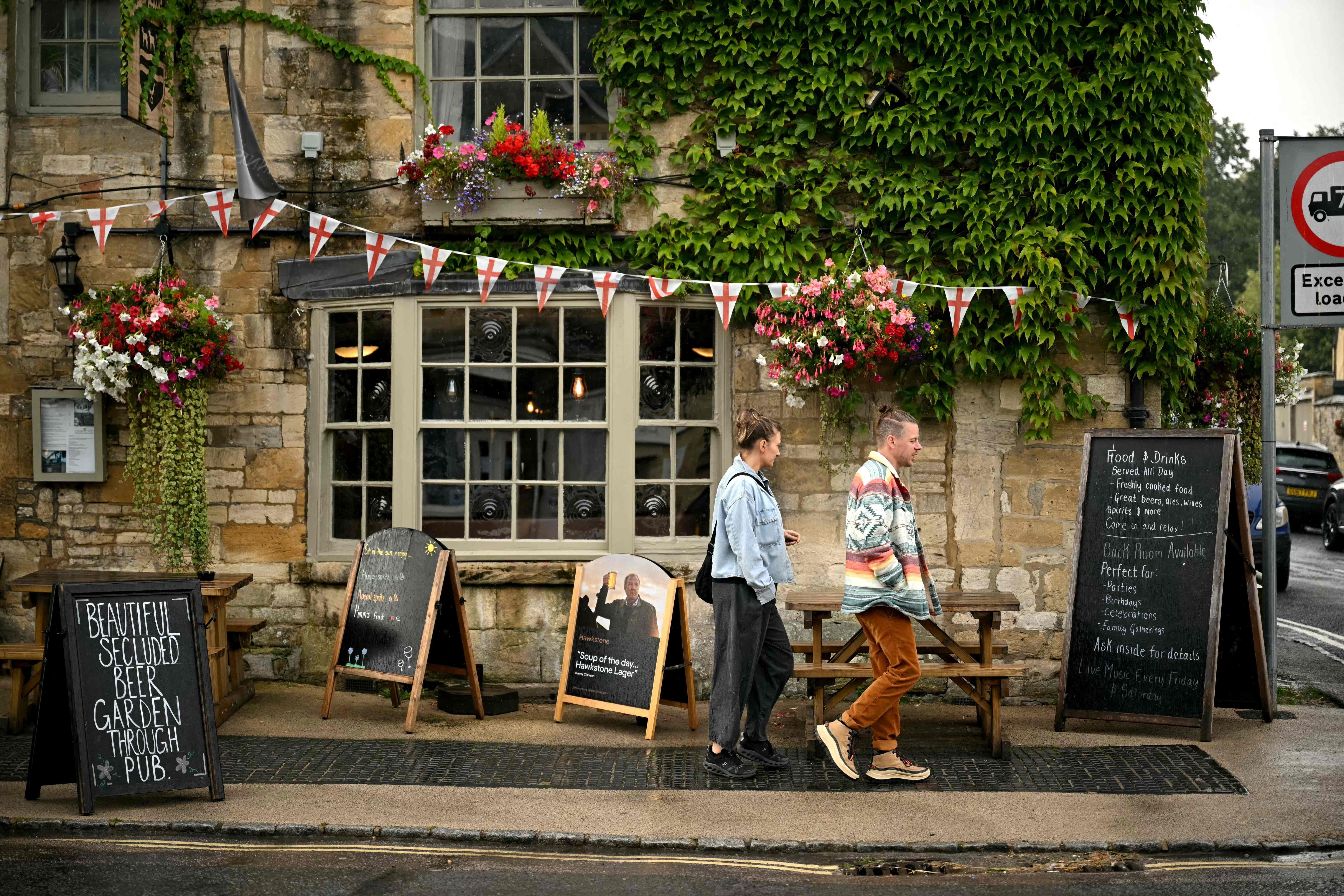 Zwei Menschen gehen an einem traditionellen, von Blumen geschmückten Pub in Burford vorbei.